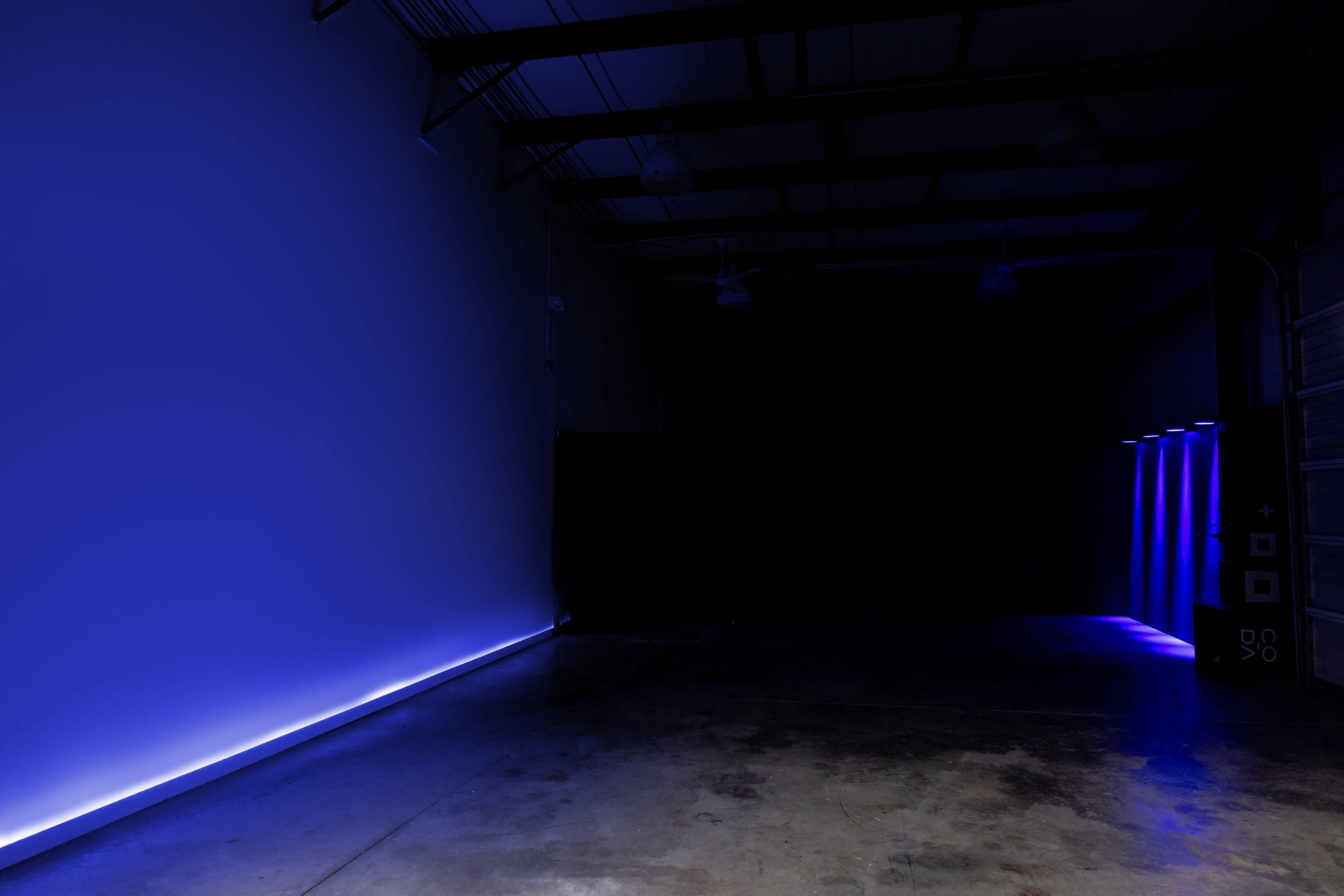 A dimly lit industrial space with a bright blue light strip along one wall and faint light sources in the background.