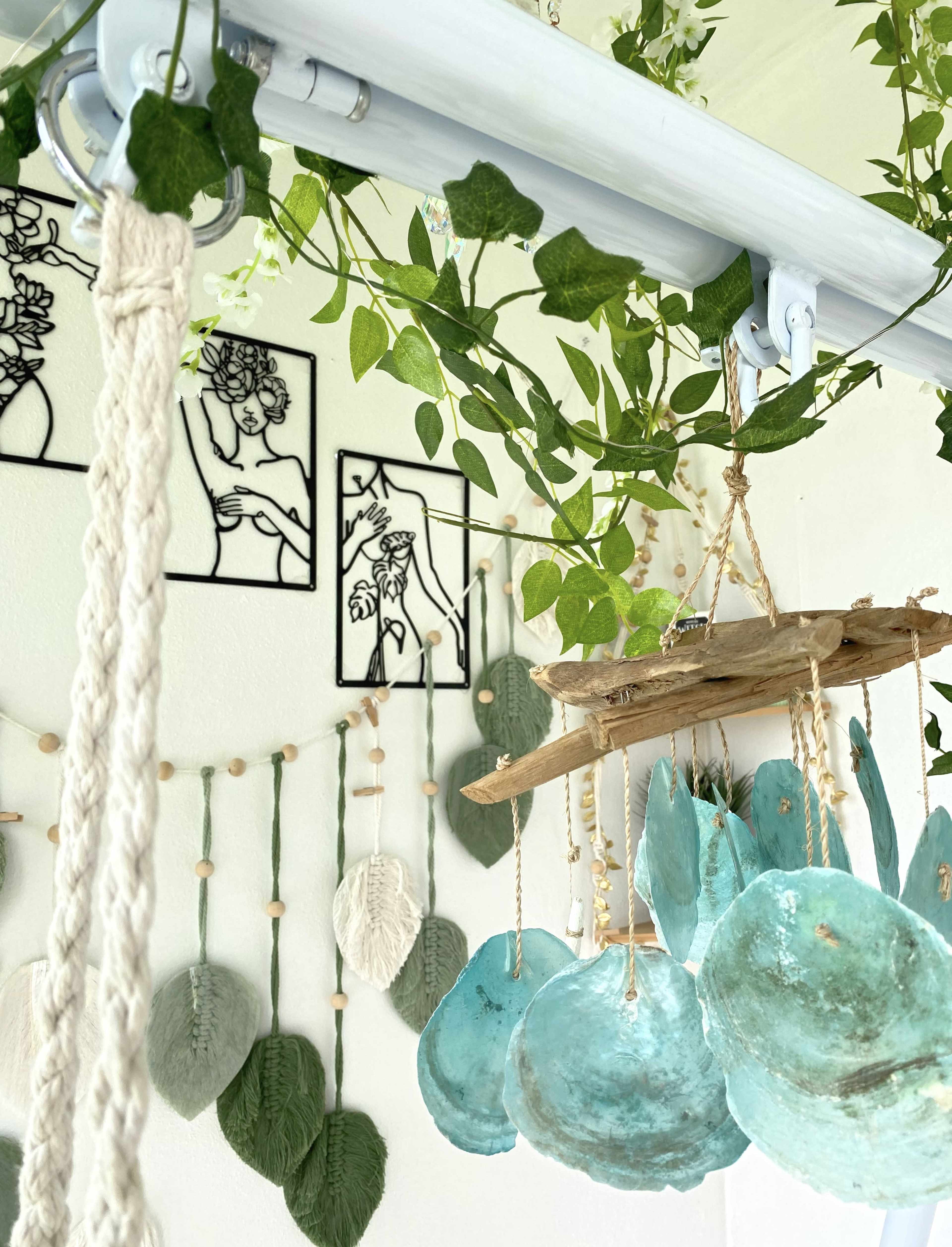 A decorative wall with hanging plants, framed artwork, and a mobile made of circular turquoise pieces suspended from a wooden base.