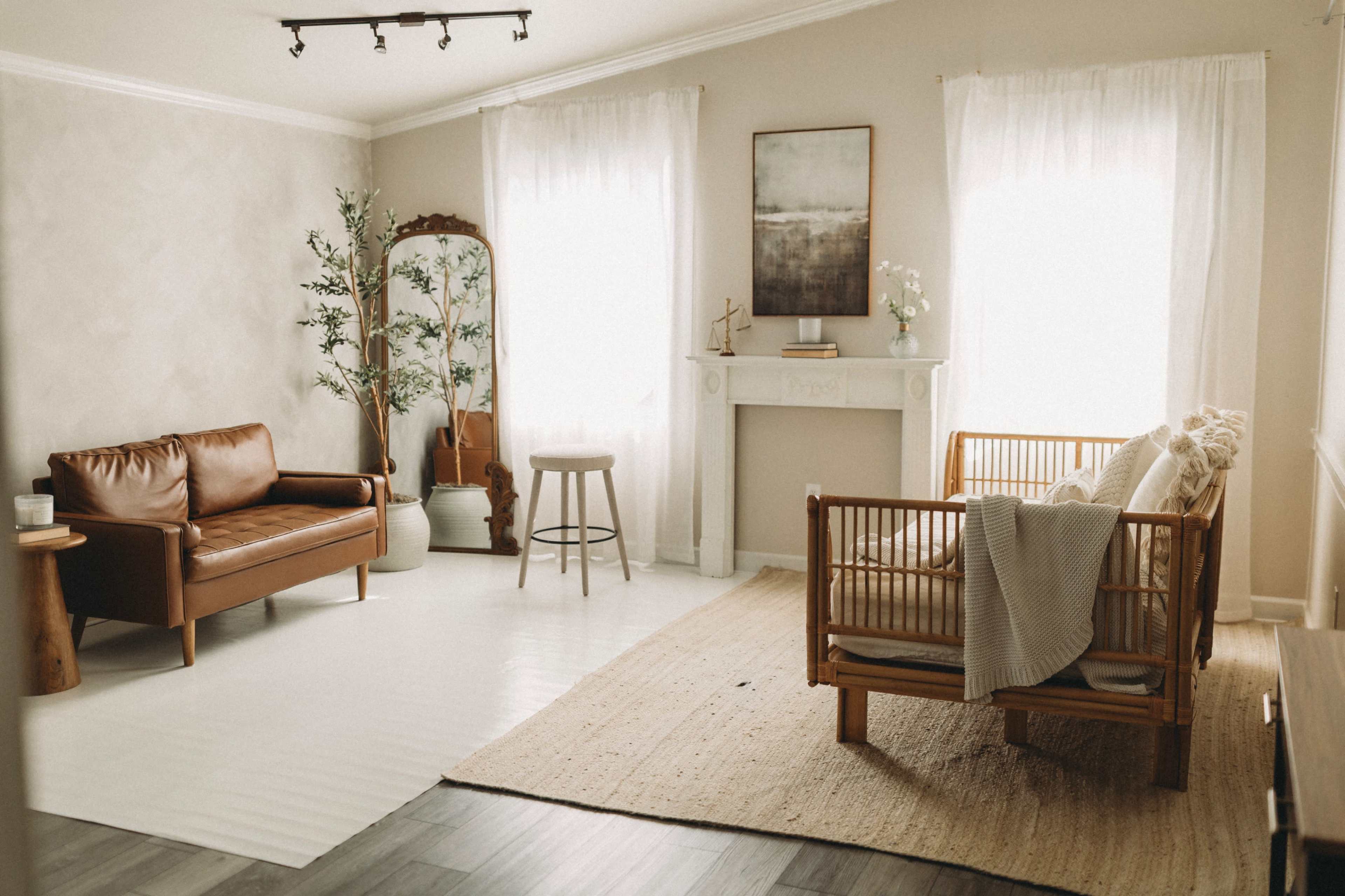 The image shows a cozy living room with a brown leather sofa, a wooden armchair, a minimalist fireplace, and large windows letting in natural light.