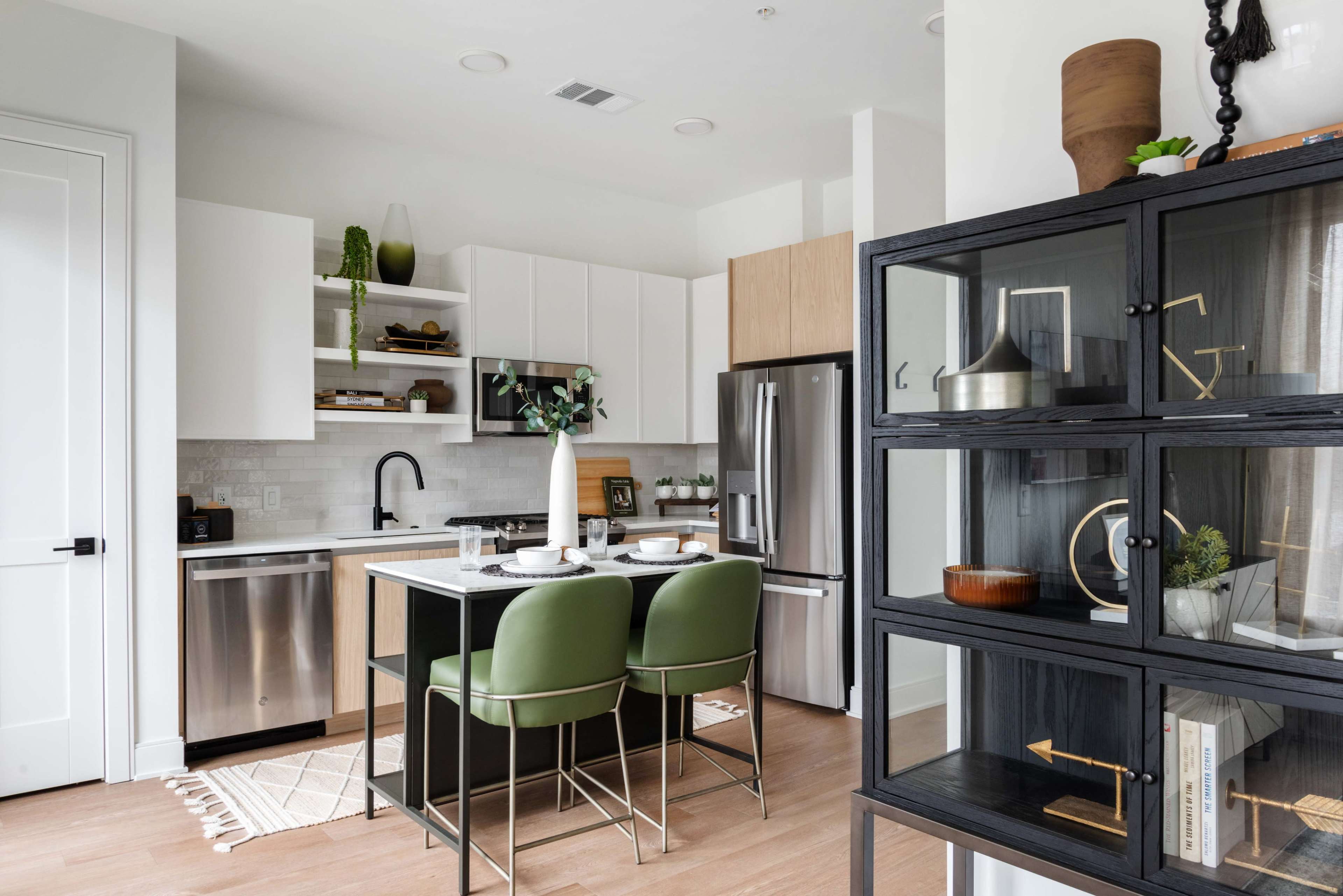 The image shows a modern kitchen with a central island, stainless steel appliances, white cabinetry, and a glass display cabinet in the foreground.