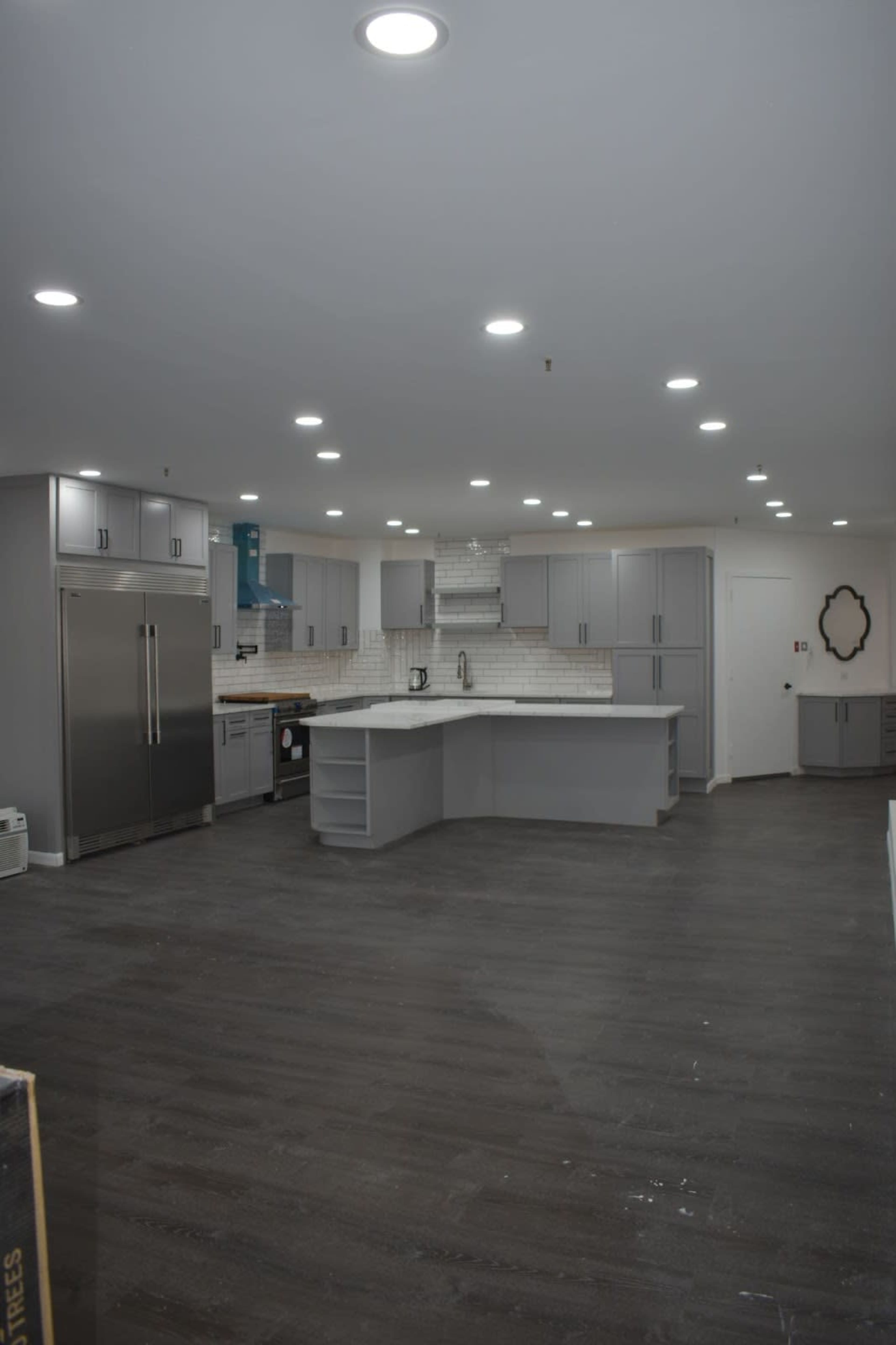 A spacious kitchen with gray cabinetry, an island countertop, and modern appliances set on dark wooden flooring.