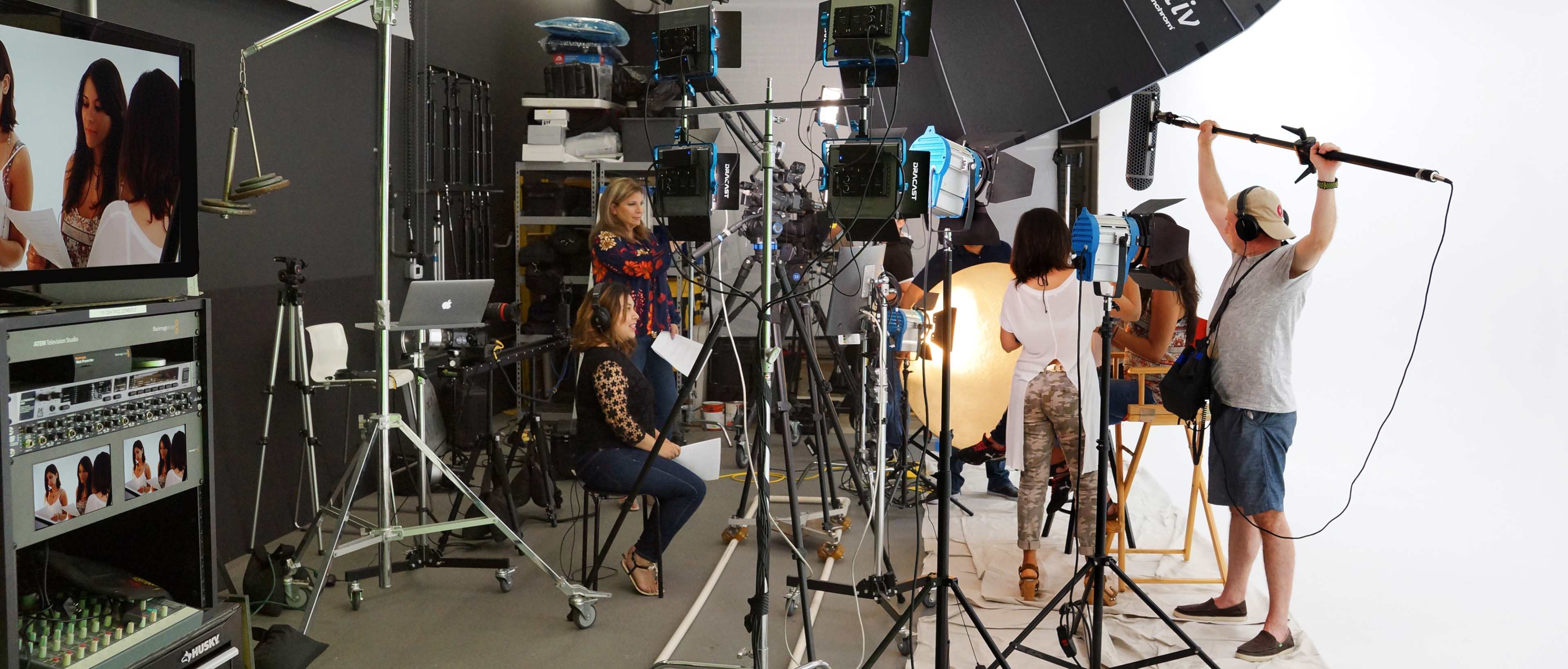 A photography studio is set up for a shoot, featuring various lighting equipment, cameras, and a team of people preparing for a session.