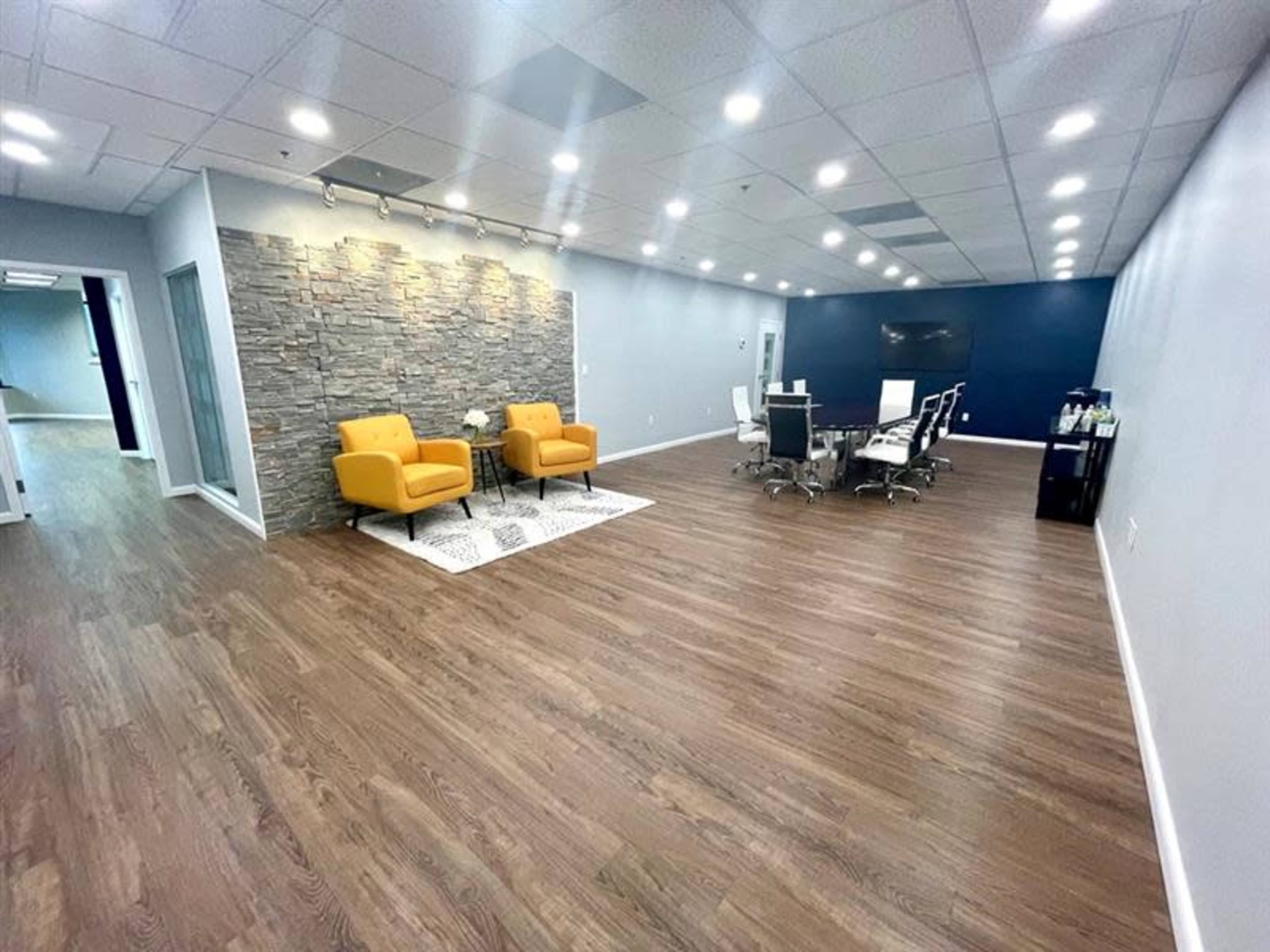 A modern office space with two yellow chairs near a stone accent wall and a conference table with chairs on a wooden floor.