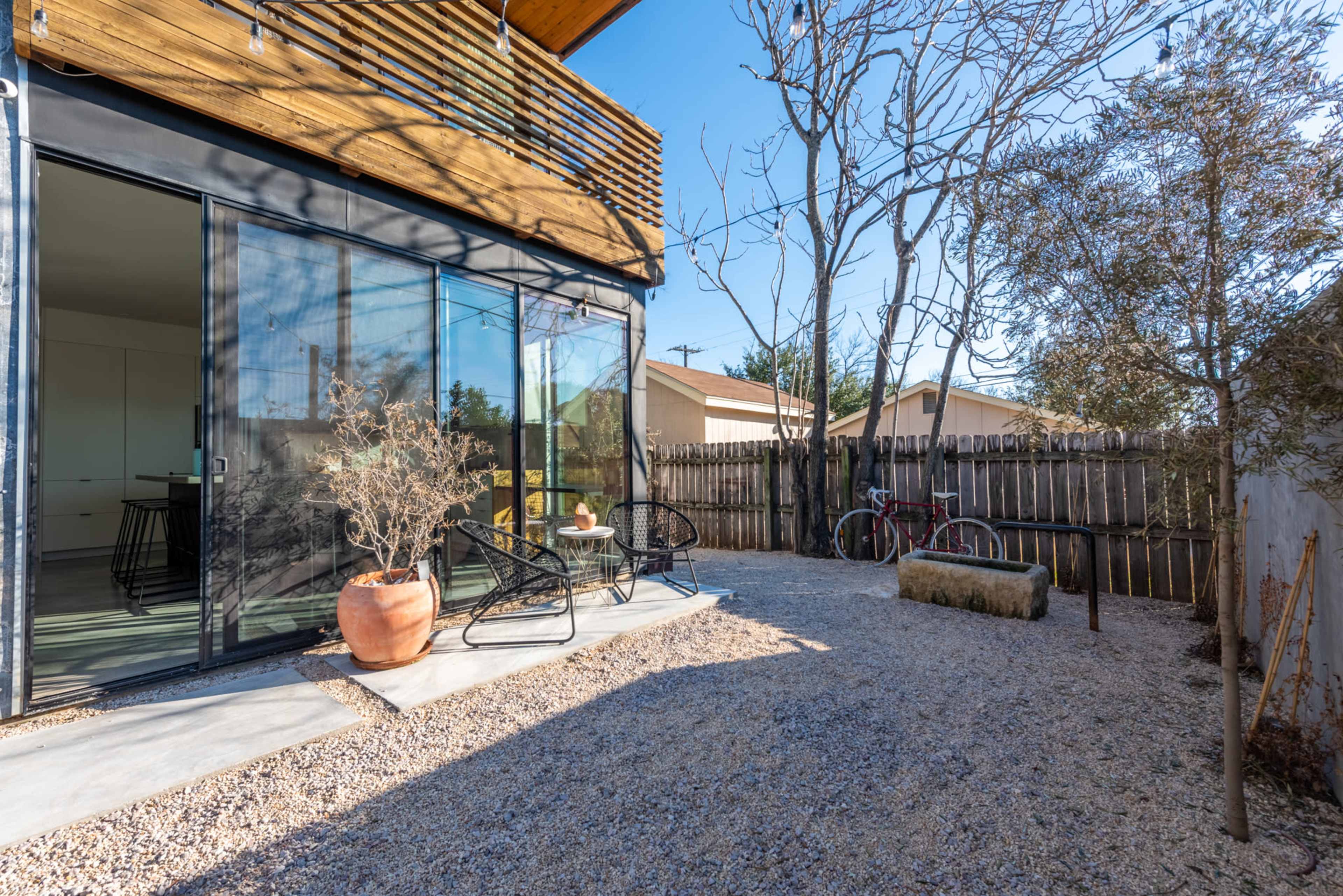 A modern outdoor patio features gravel flooring, a black metal chair set, and a bicycle parked near a wooden fence.