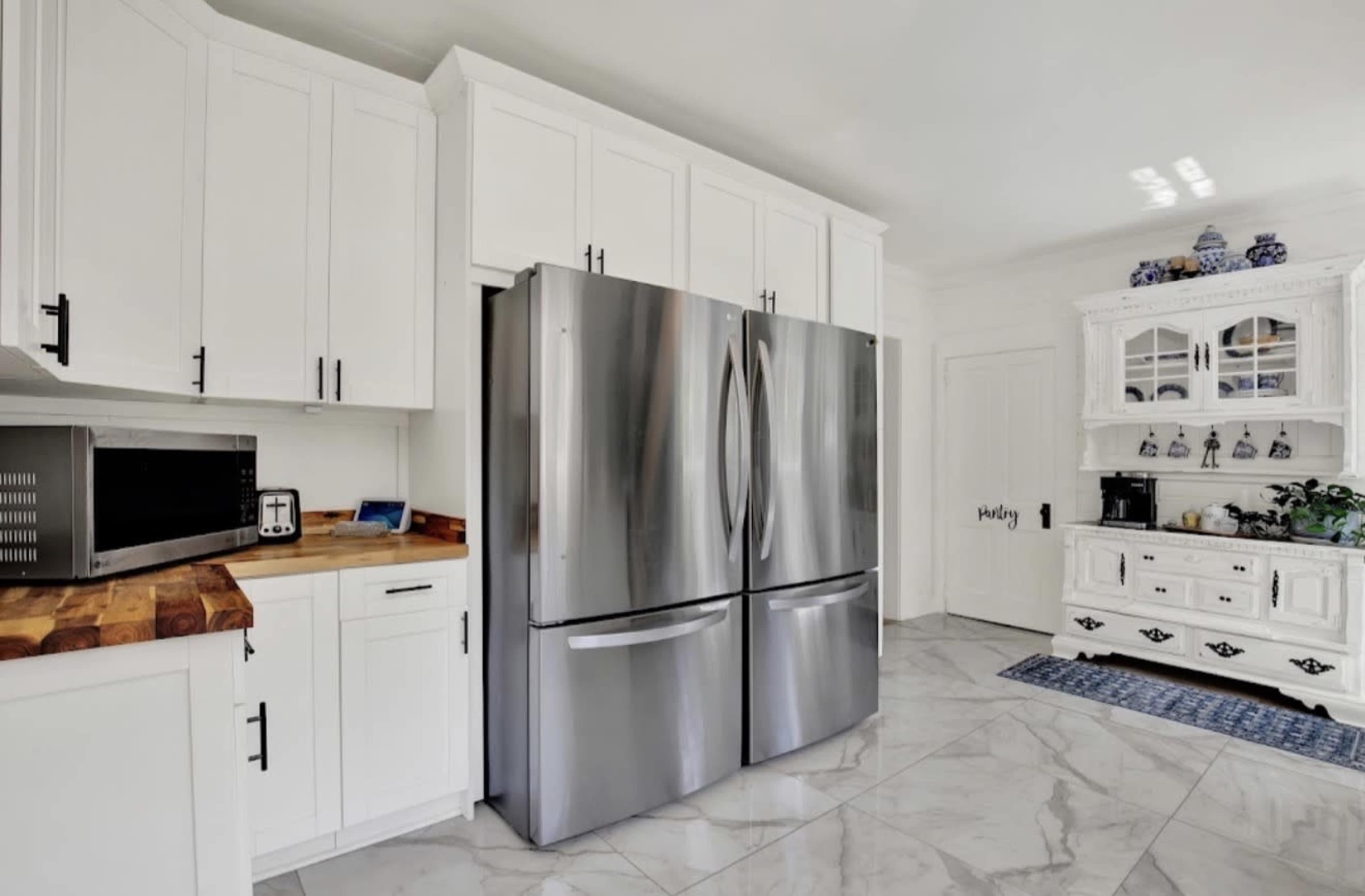 The image shows a modern kitchen with white cabinetry, a stainless steel refrigerator, and a decorative wooden sideboard.