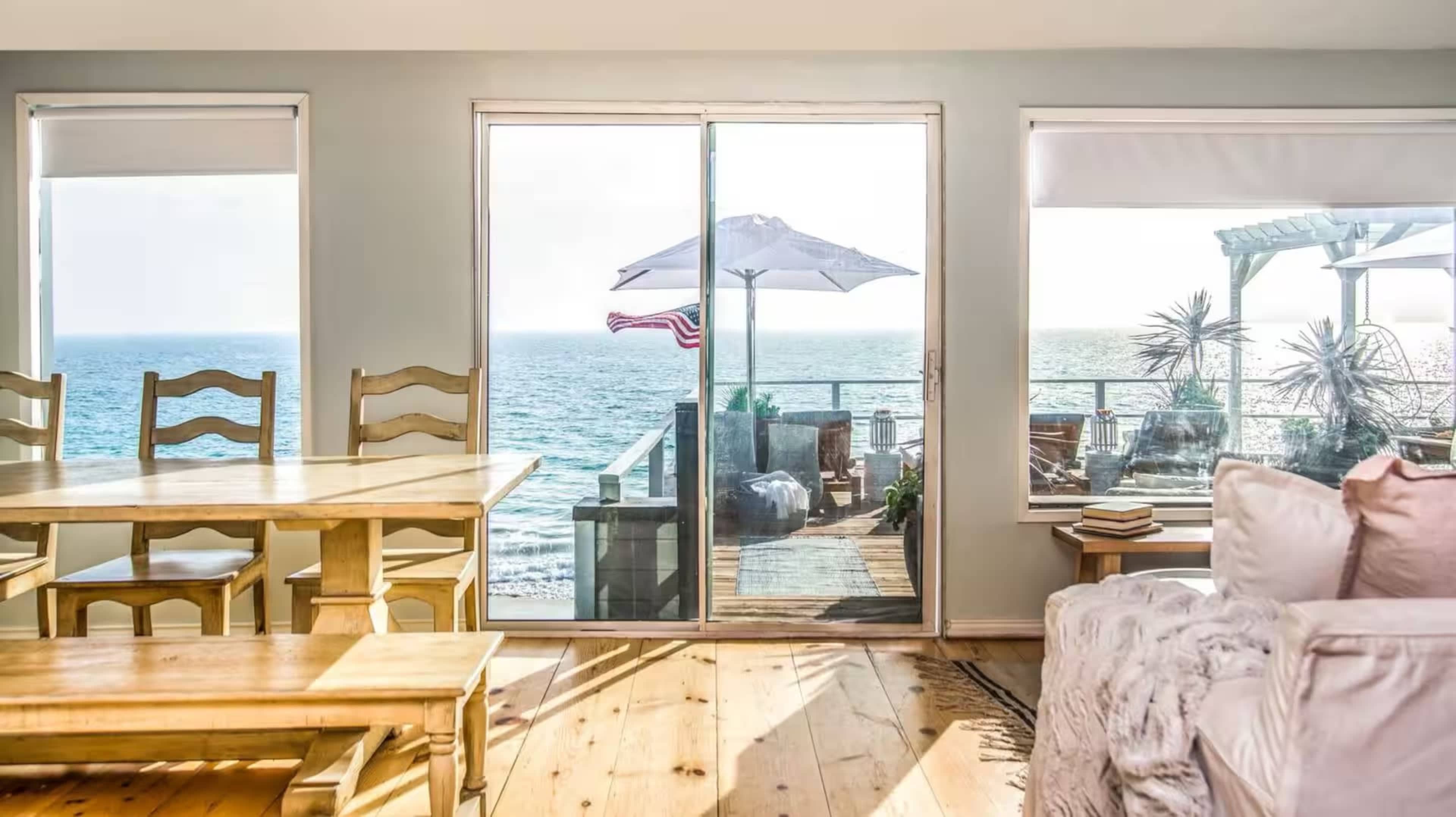 A beachside living area features a dining table and chairs, with sliding glass doors leading to a deck overlooking the ocean.