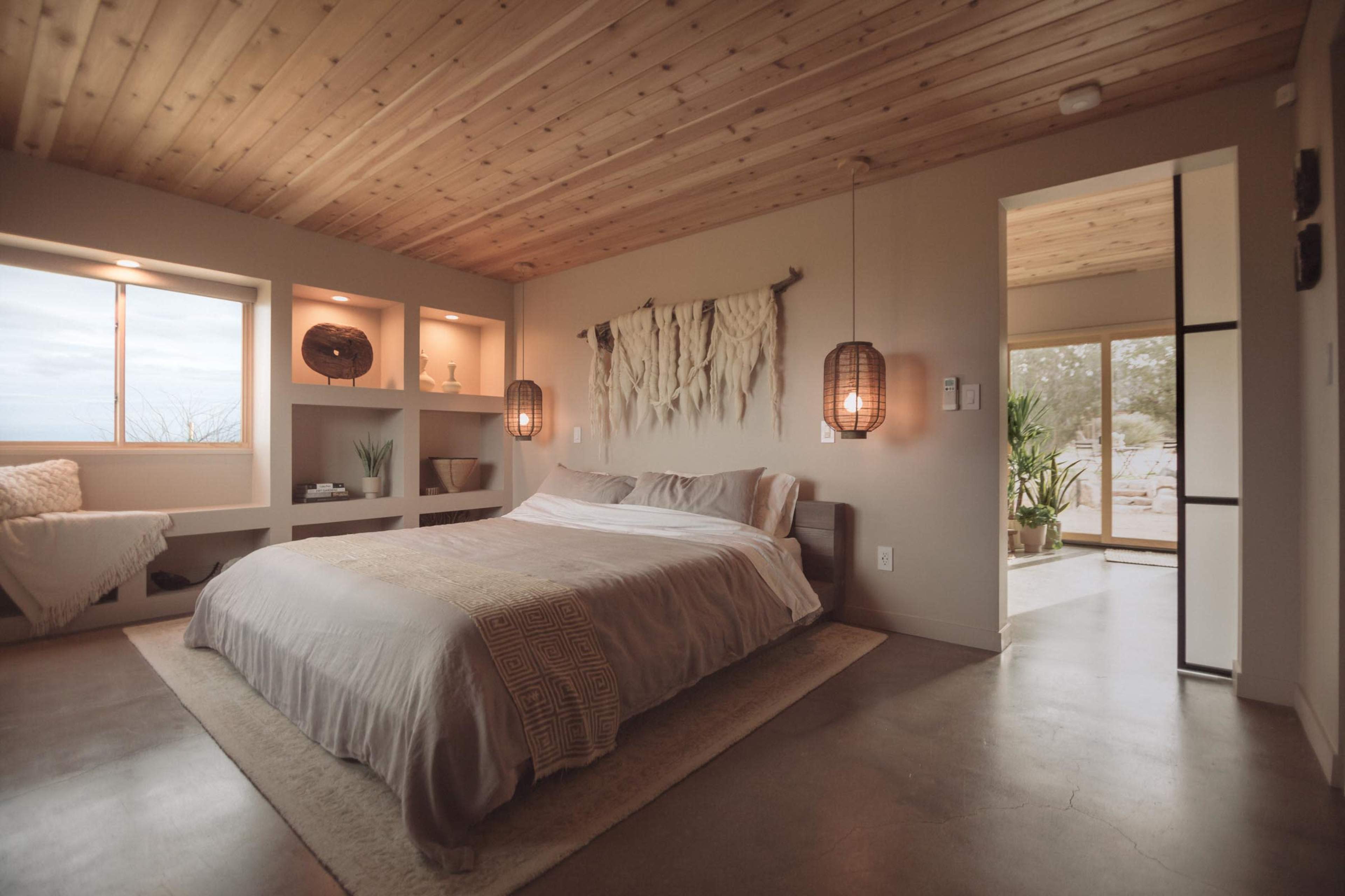 A minimalist bedroom featuring a bed with neutral bedding, wooden ceiling, and wall-mounted shelves with decorative items.