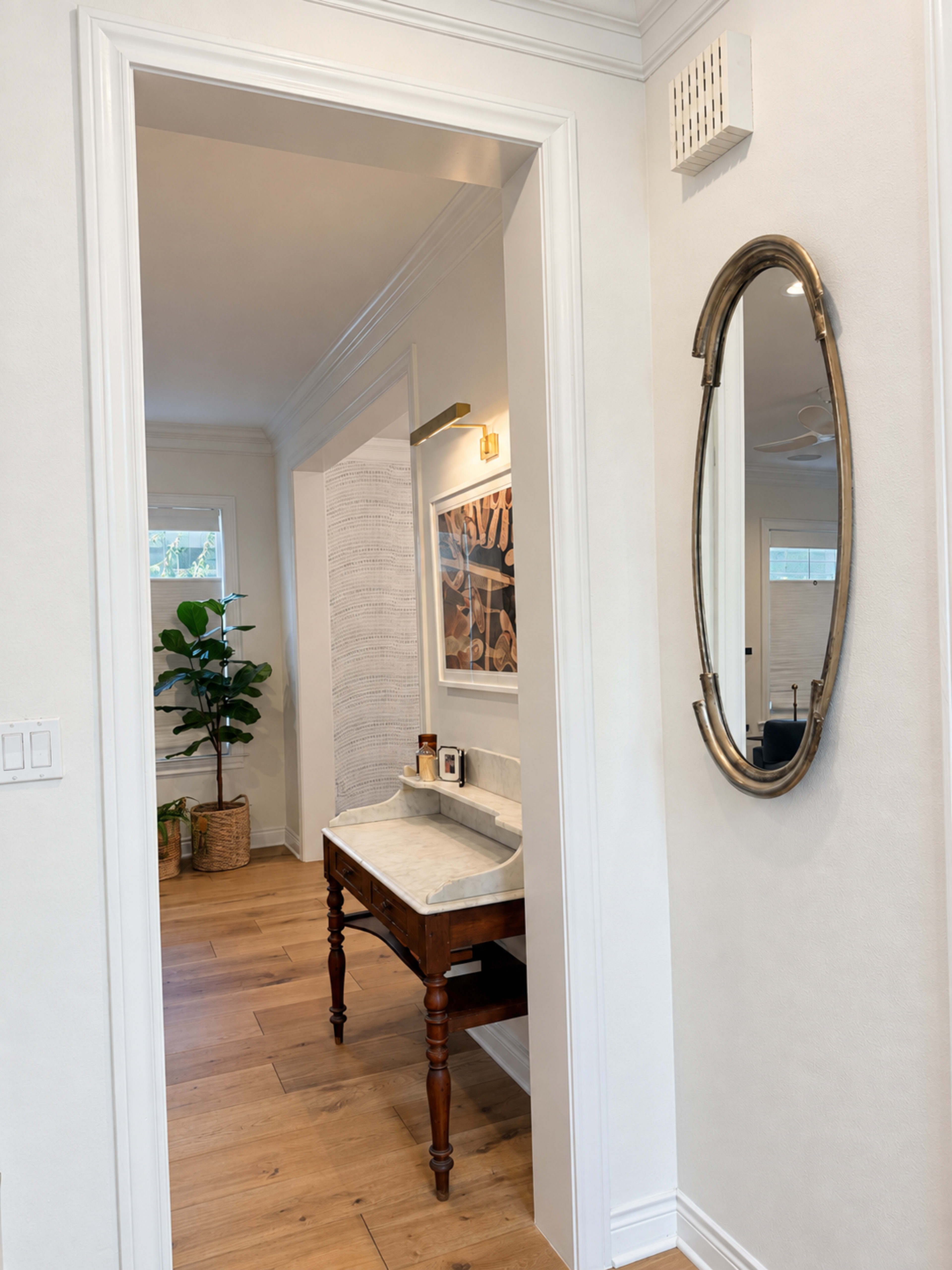 A well-lit hallway leads to a bathroom featuring a marble-topped vanity and a decorative mirror on the wall.