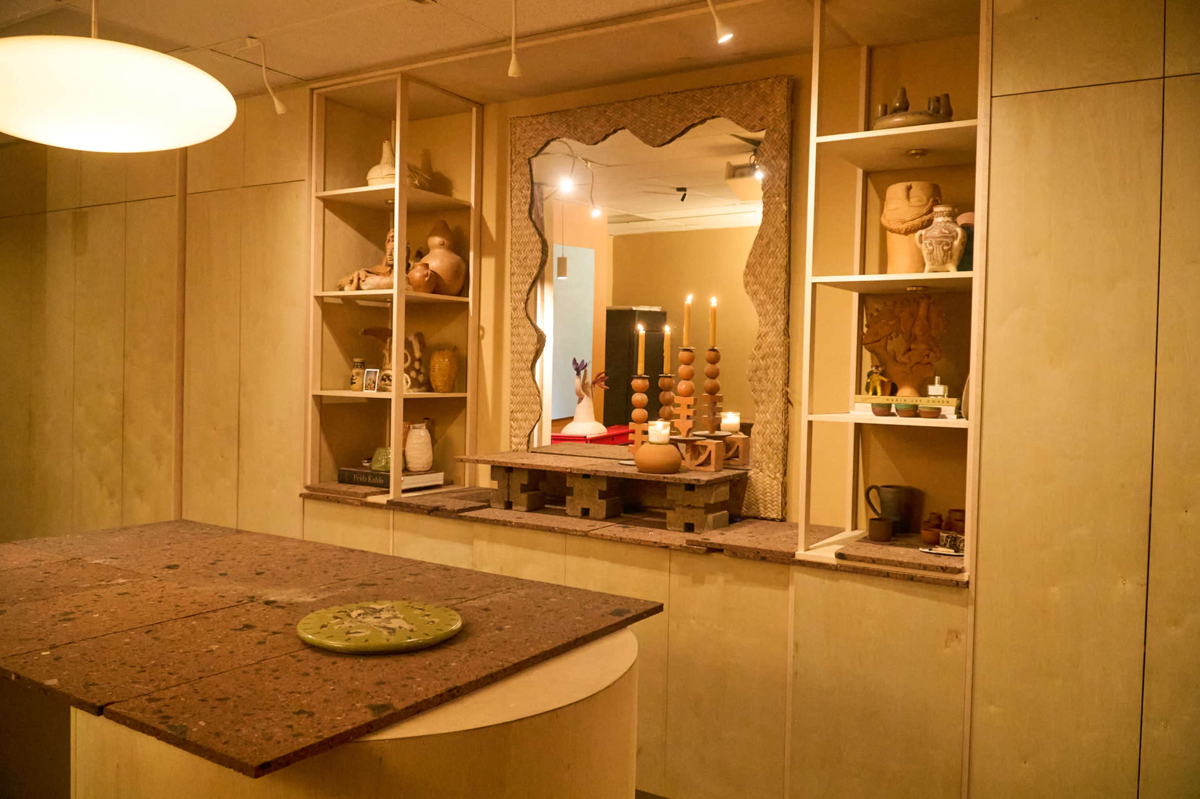 The image shows a minimalist interior with light wood shelves displaying pottery and decorative items, and a table centerpiece featuring candles and an arrangement of objects.