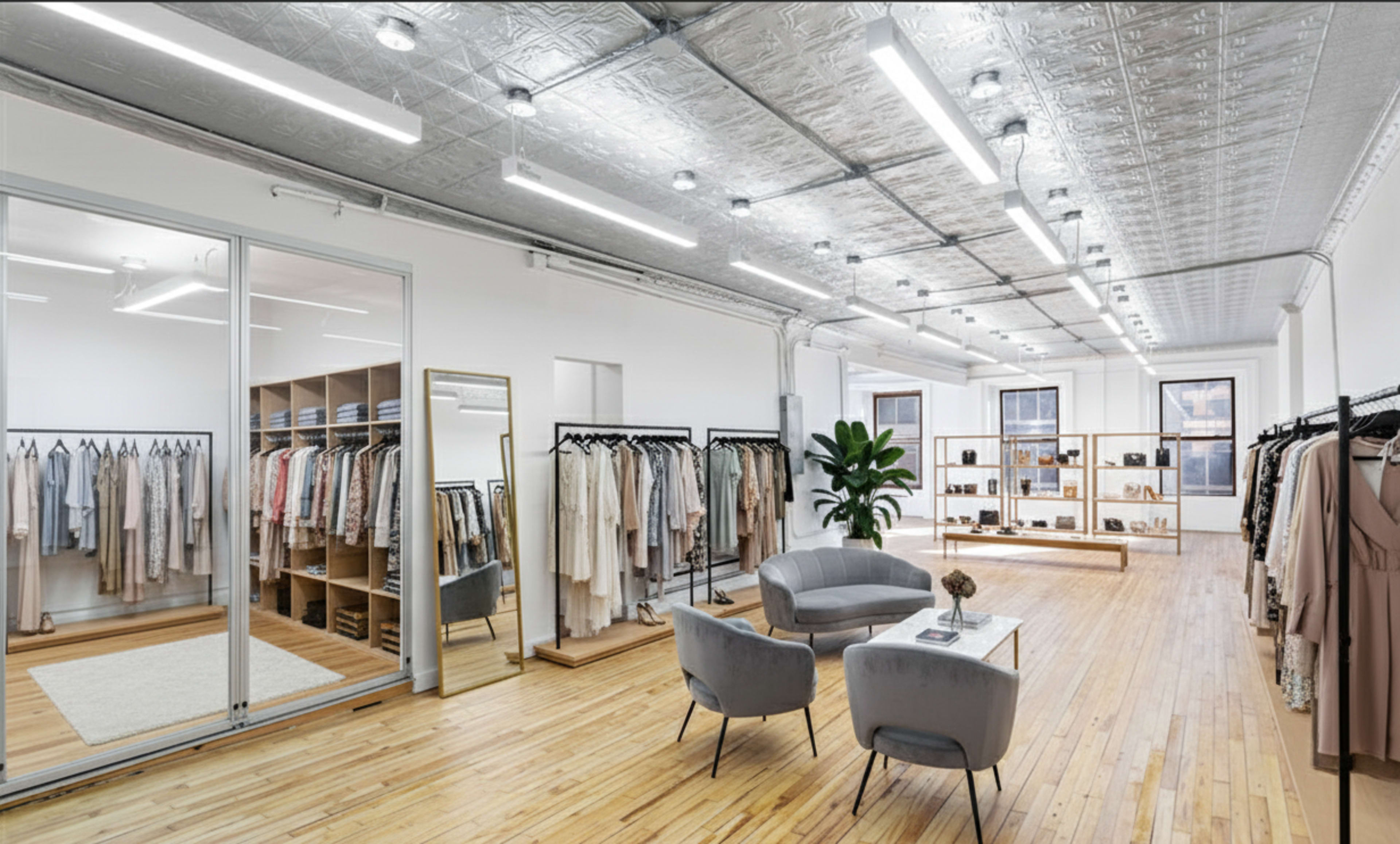 The interior of a modern clothing boutique displays rows of neatly hung garments, a seating area with two gray chairs, and stylish shelving units filled with accessories.