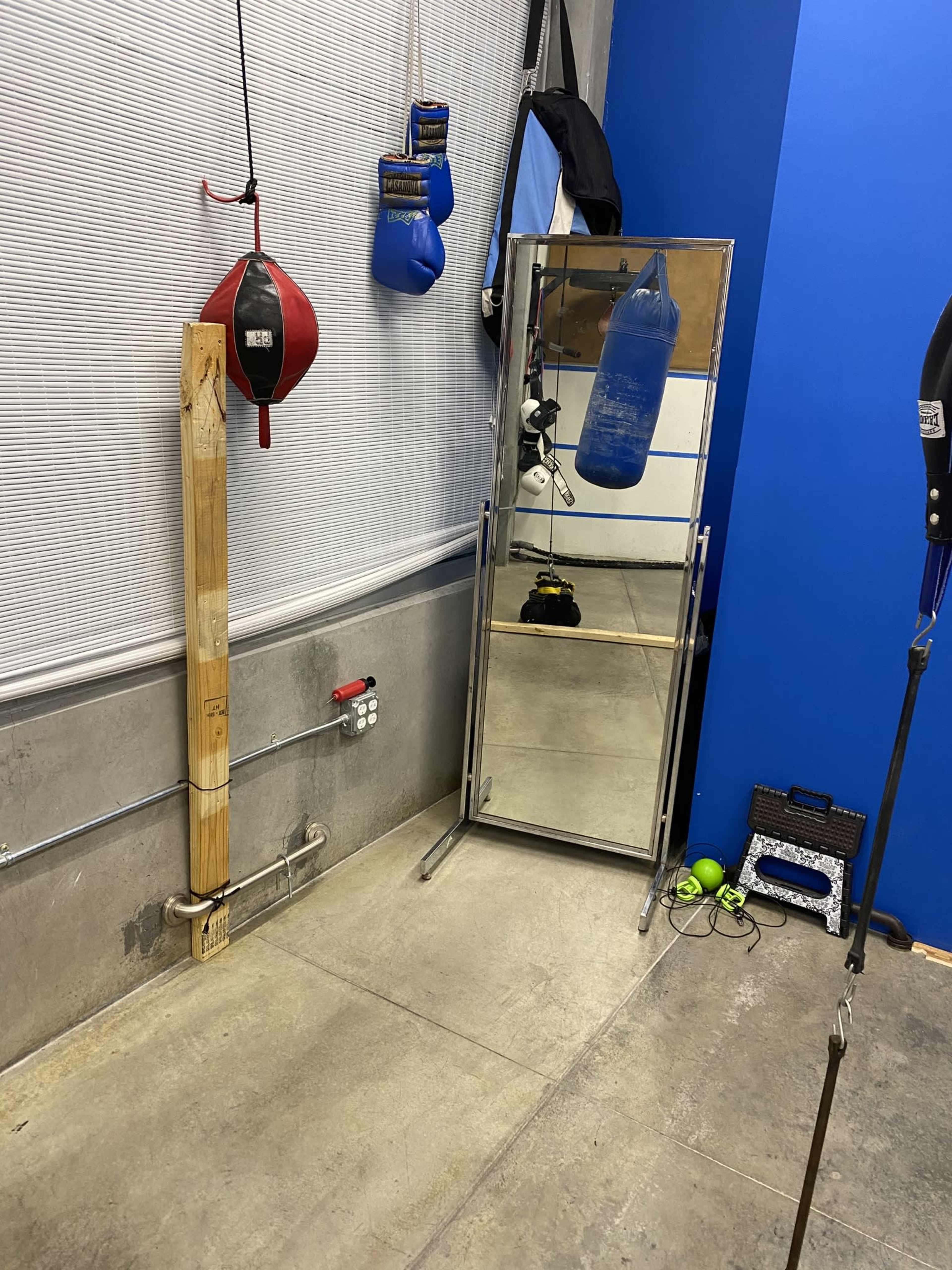 A gym corner featuring a mirror, boxing gloves, a punching bag, and various training equipment against a blue wall.