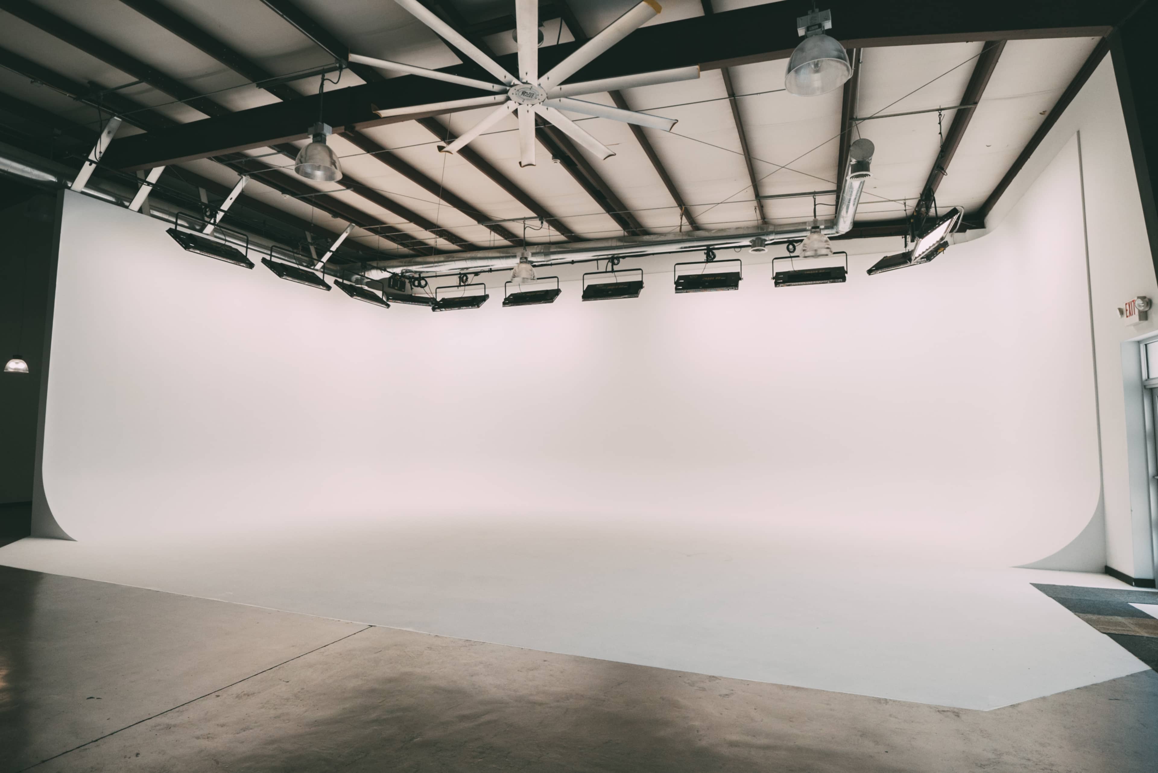 A spacious, empty studio with a seamless white backdrop and overhead lighting.