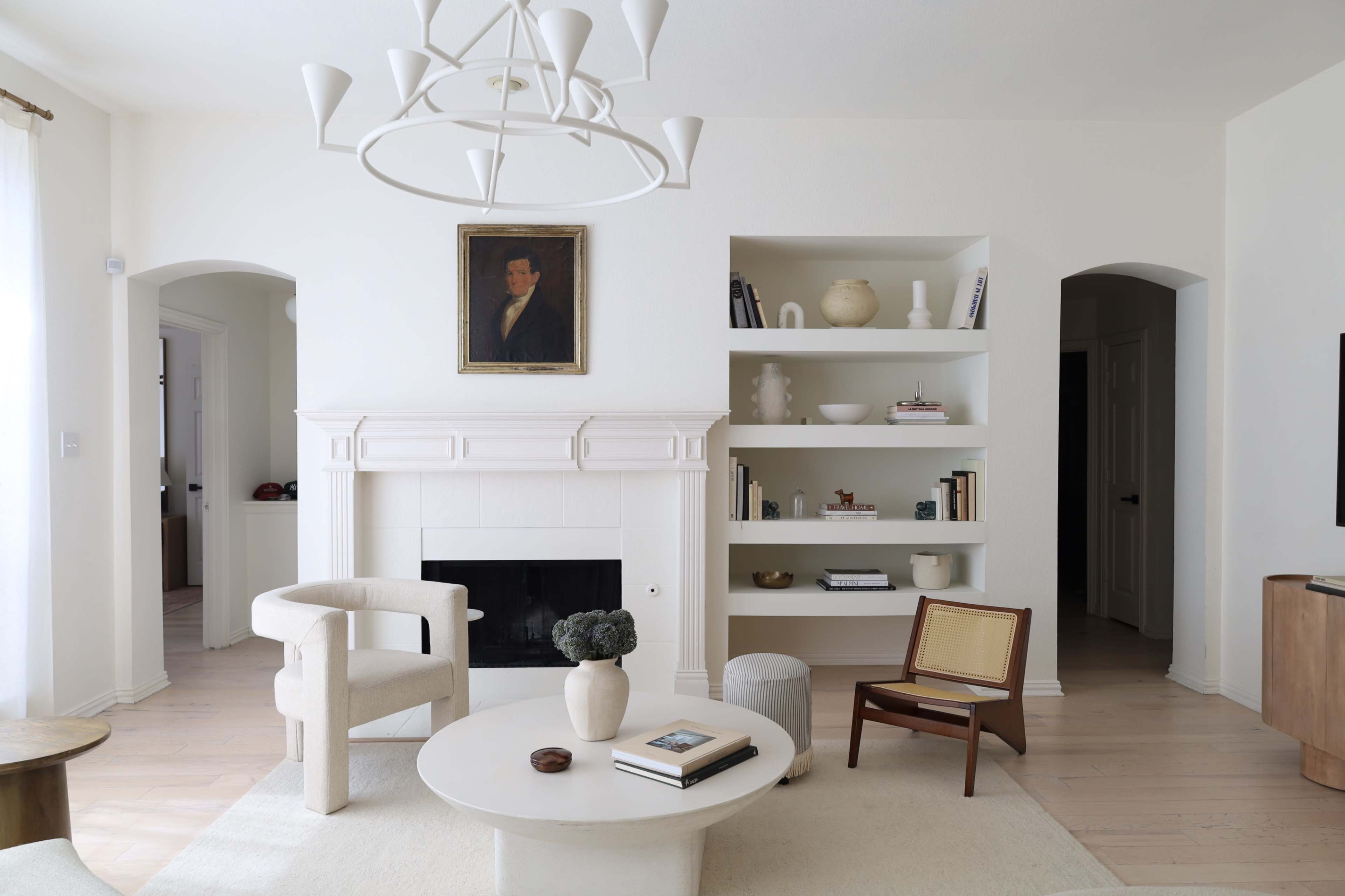 The image shows a modern living room featuring a white color palette, a fireplace, a circular coffee table, and minimalist furniture.