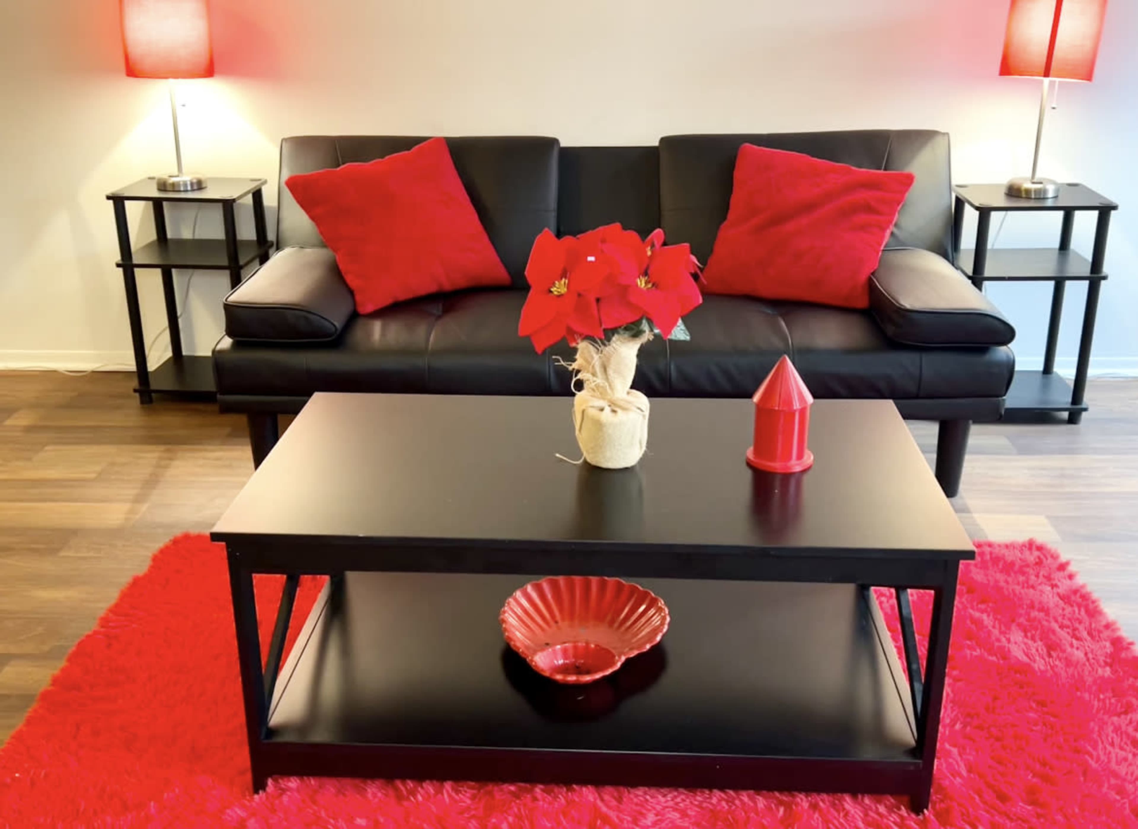 A living room with a black sofa, red cushions, a black coffee table decorated with red items, and a red rug.