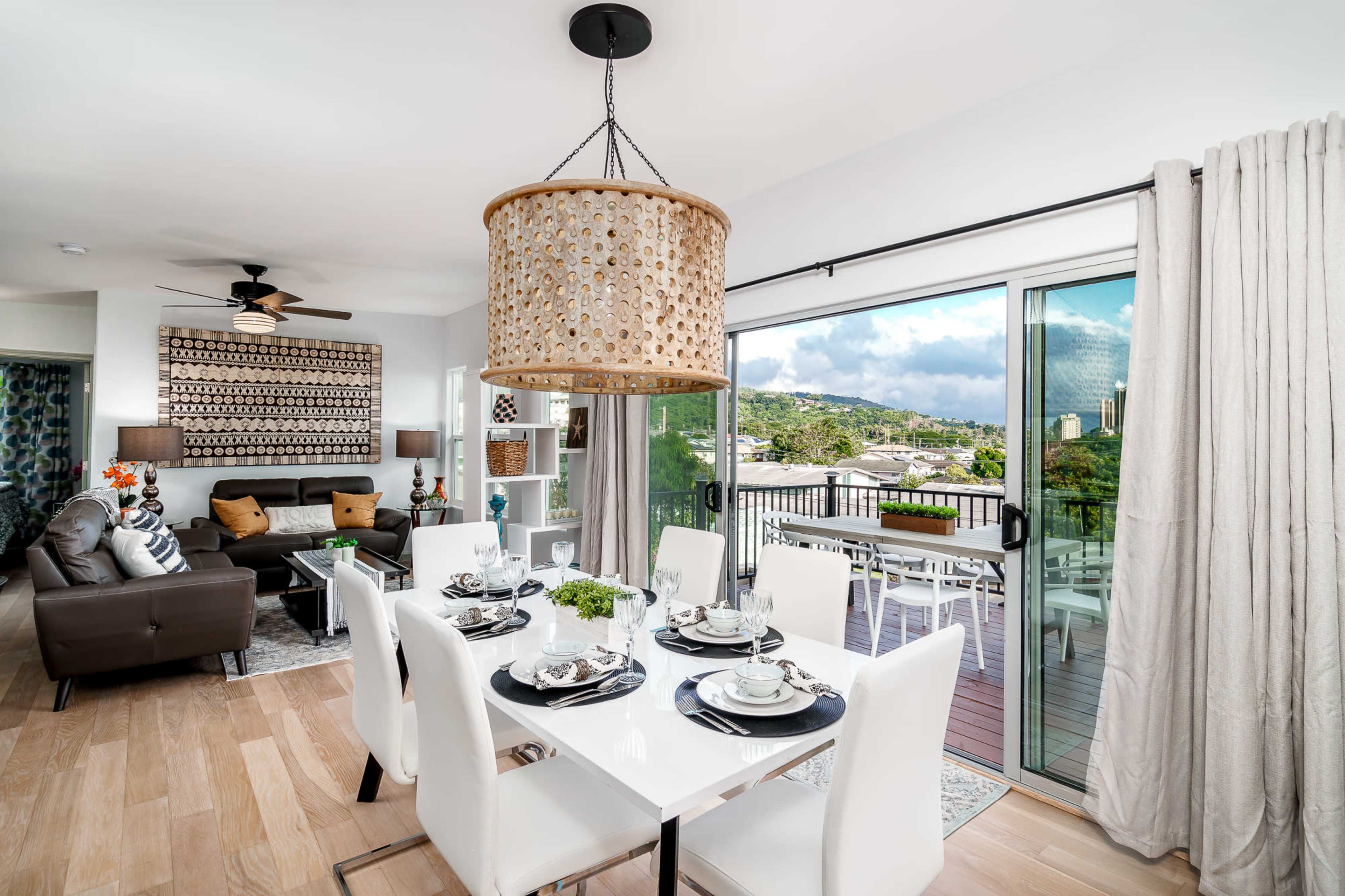 A modern dining area features a white table set for six, surrounded by white chairs, with a large sliding door revealing a view of the outdoors.