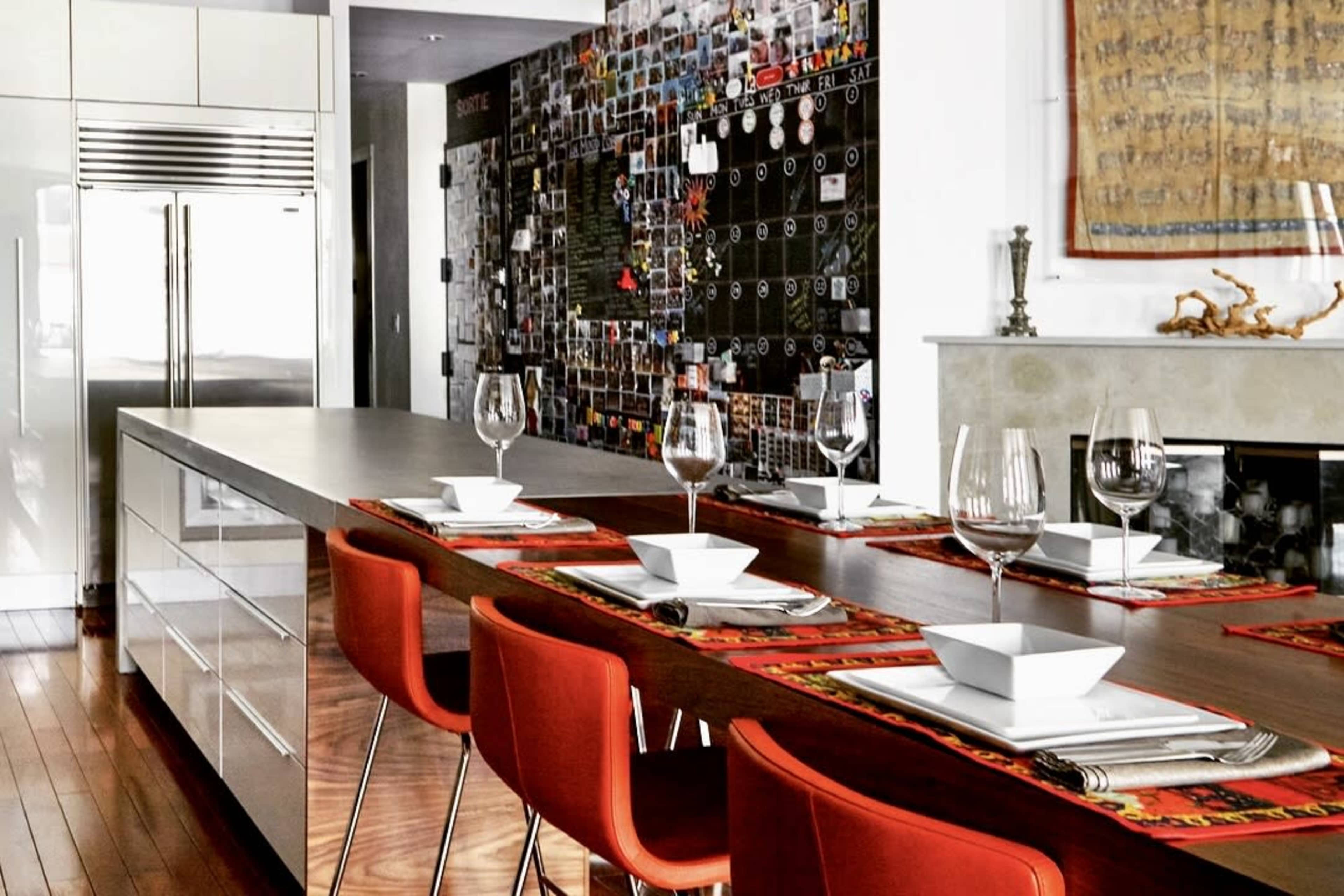 A modern kitchen features a long wooden island with red chairs and a wall decorated with various photographs and memorabilia.