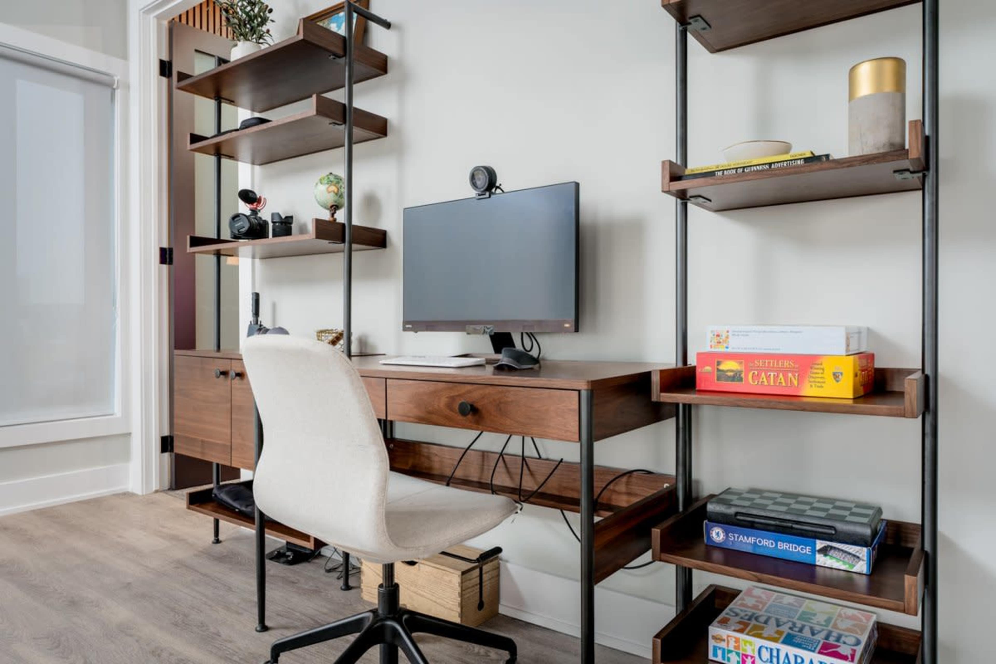 A modern home office features a desk with a computer, shelves displaying various items, and a comfortable chair.