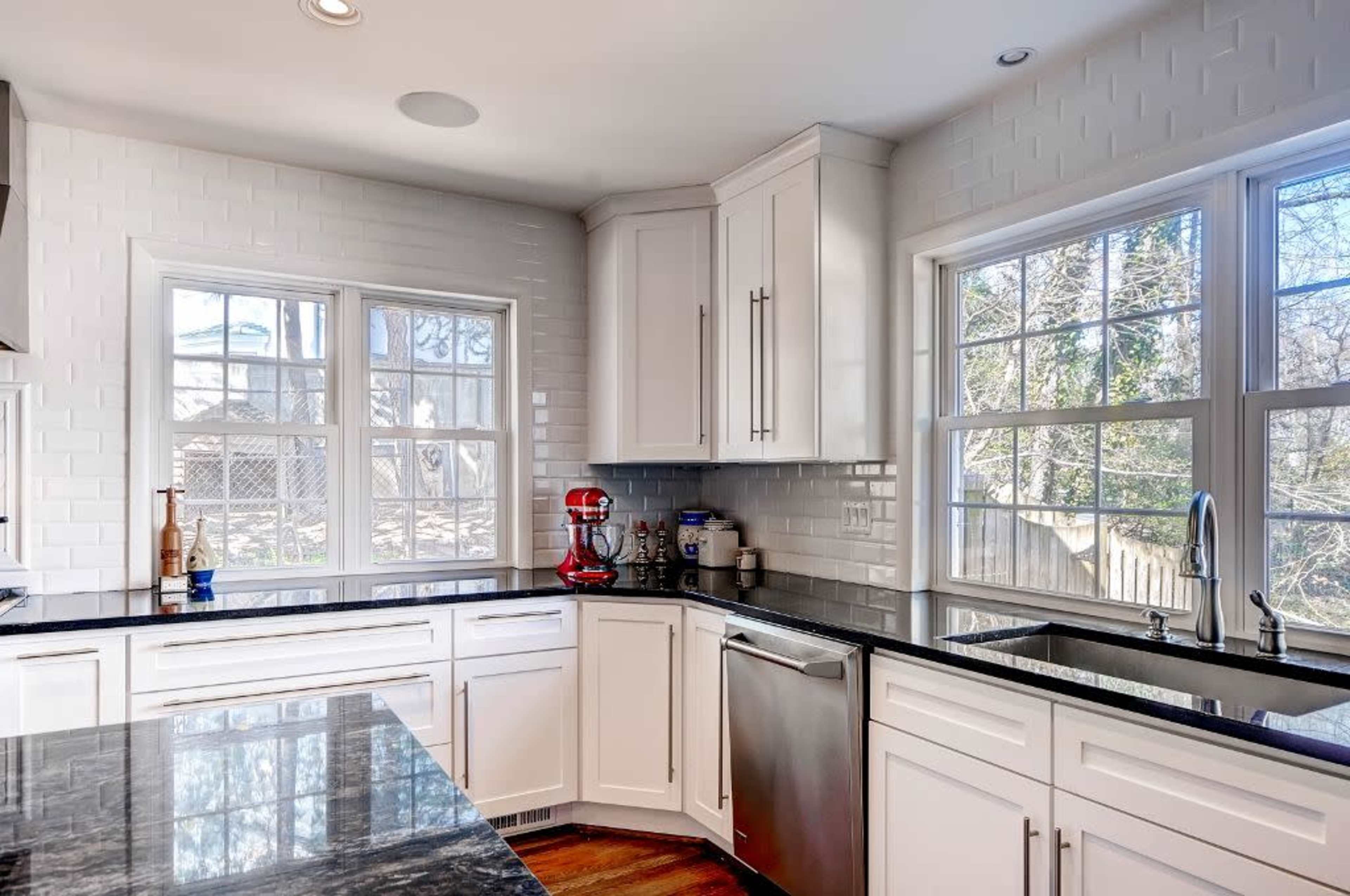 A modern kitchen with white cabinetry, a dark granite countertop, and two large windows providing natural light.