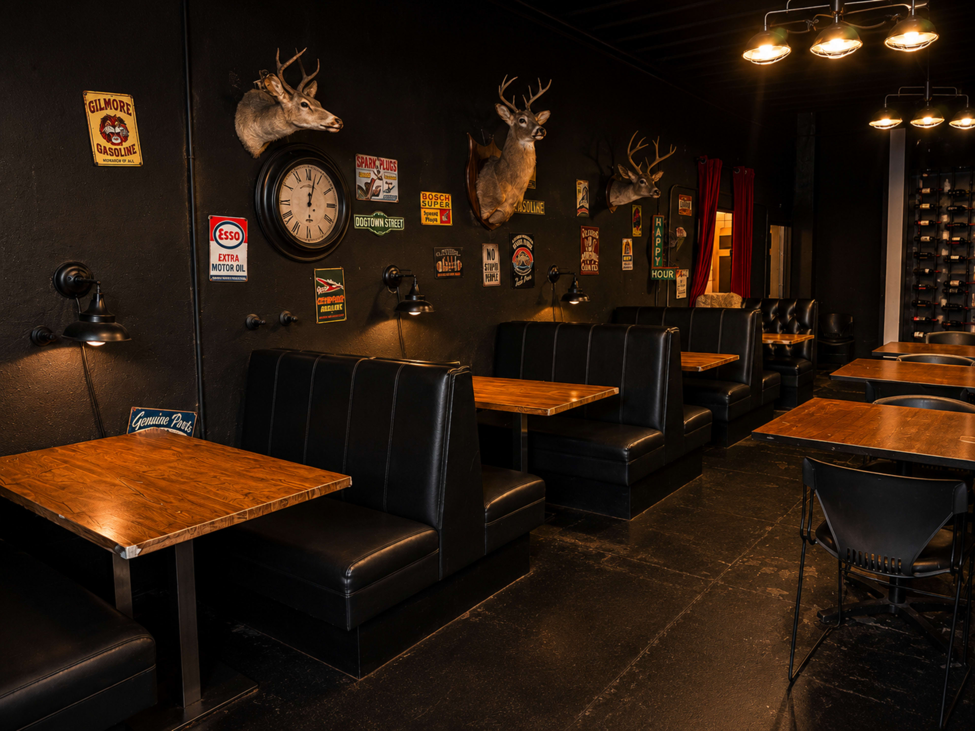 The image shows a dimly lit restaurant interior featuring wooden tables and black upholstered booths, with deer head wall decorations and various vintage signs.
