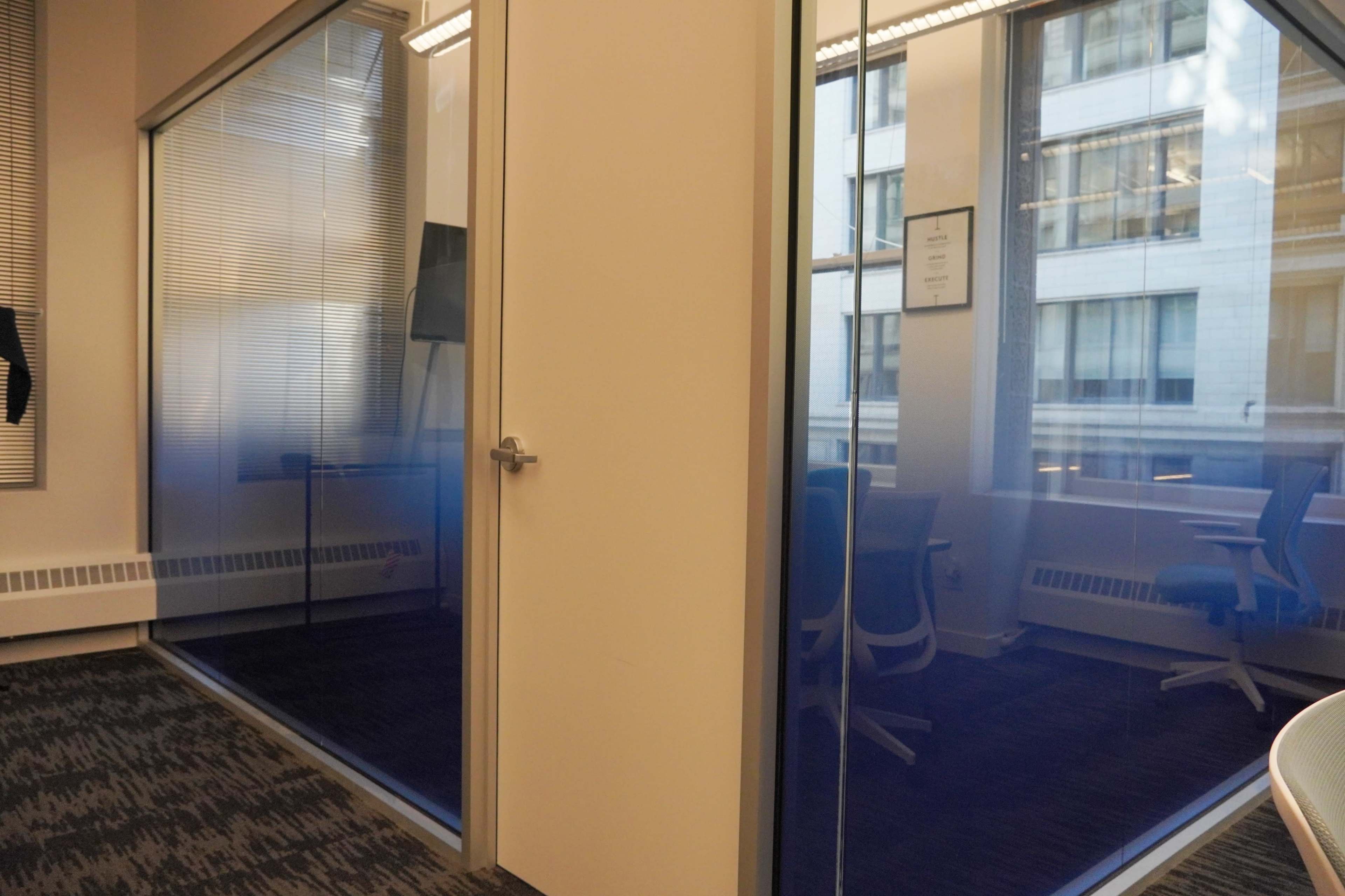 A modern office space with two glass-walled conference rooms separated by a door.