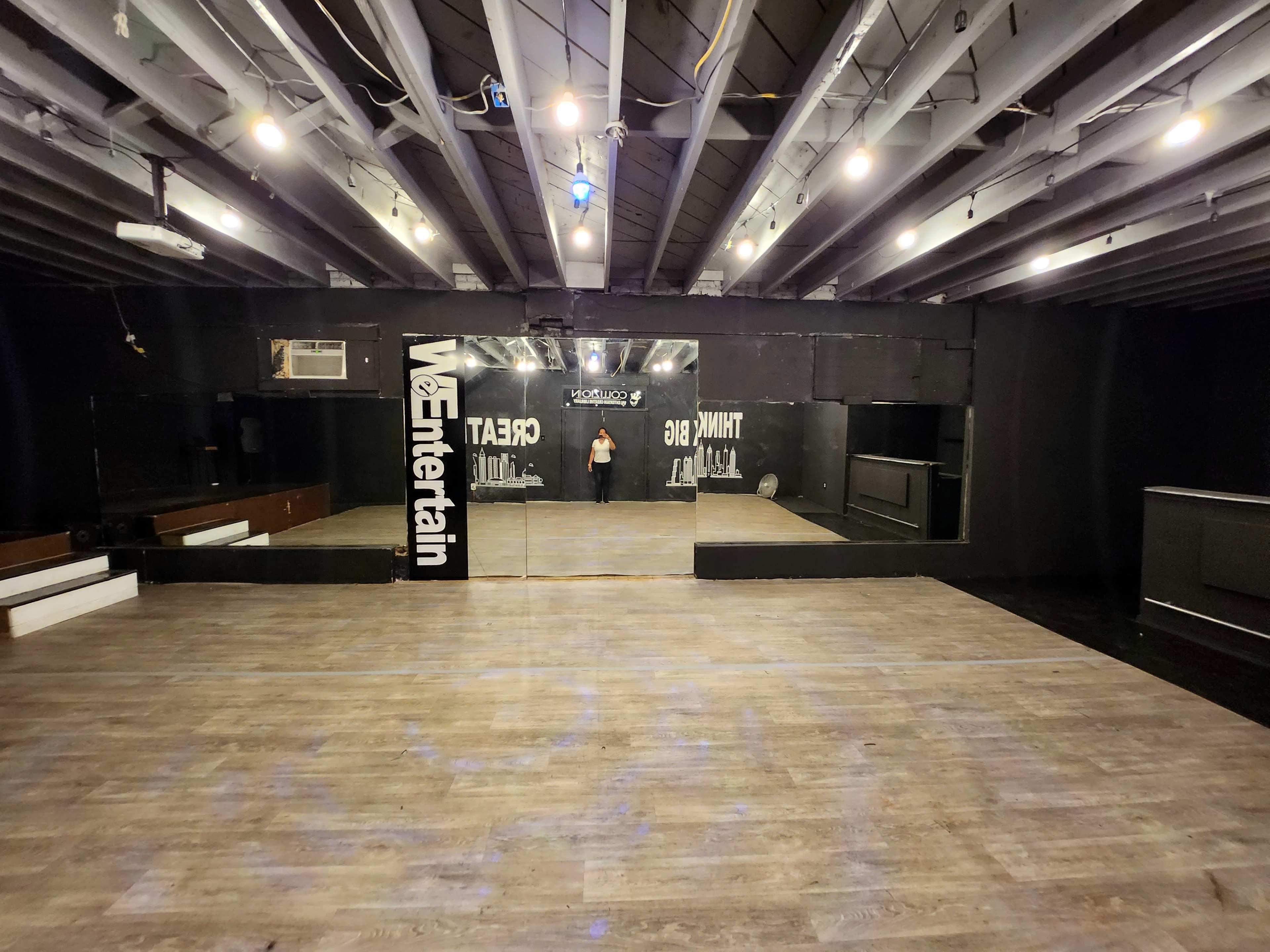 An empty dance studio with wooden flooring, mirrored walls, and overhead lights.
