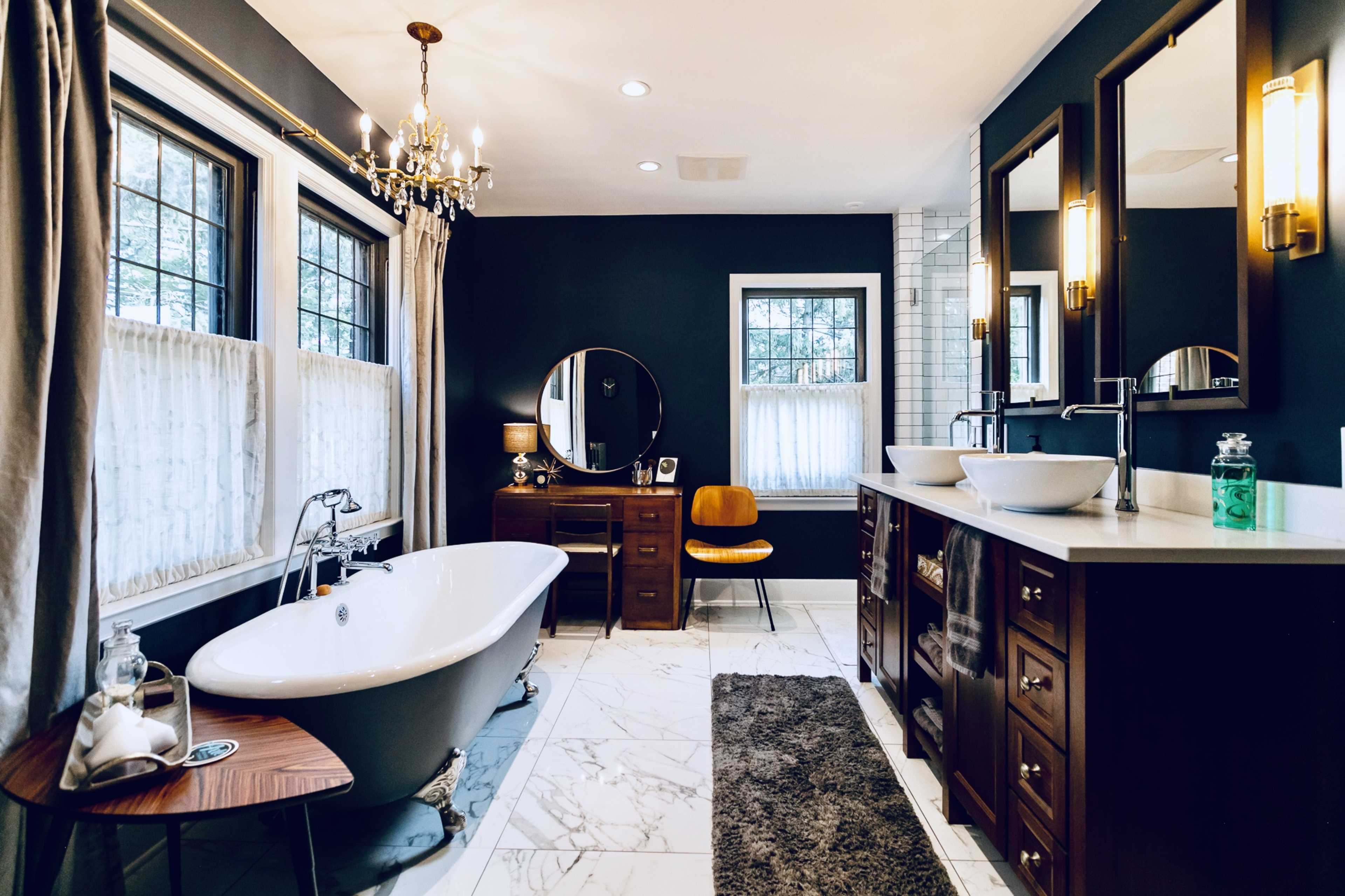 The bathroom features a freestanding bathtub, dual sinks in wooden cabinetry, and large windows allowing natural light.