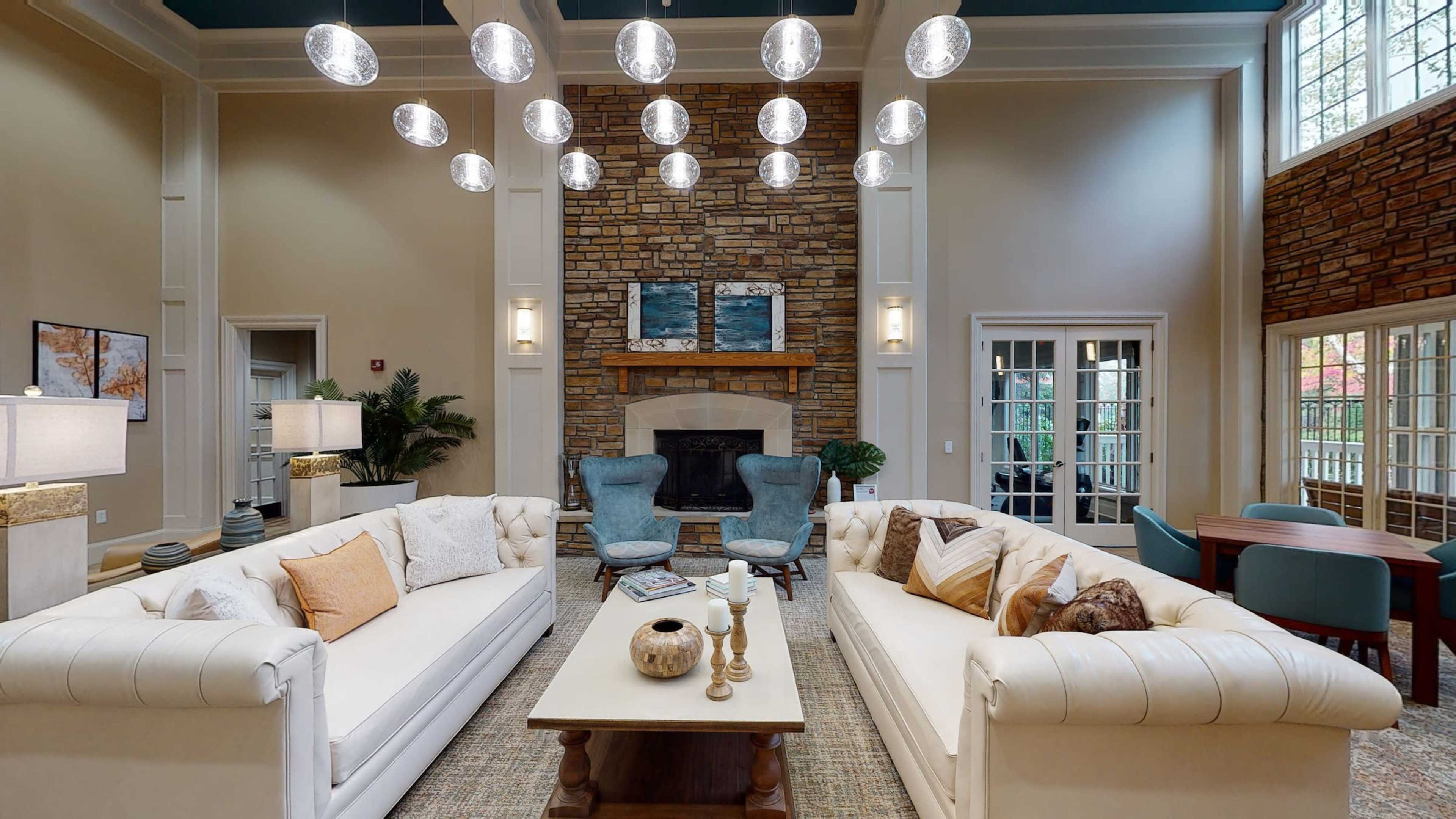 A spacious living area features two white tufted sofas, a stone fireplace, and a collection of modern hanging light fixtures.