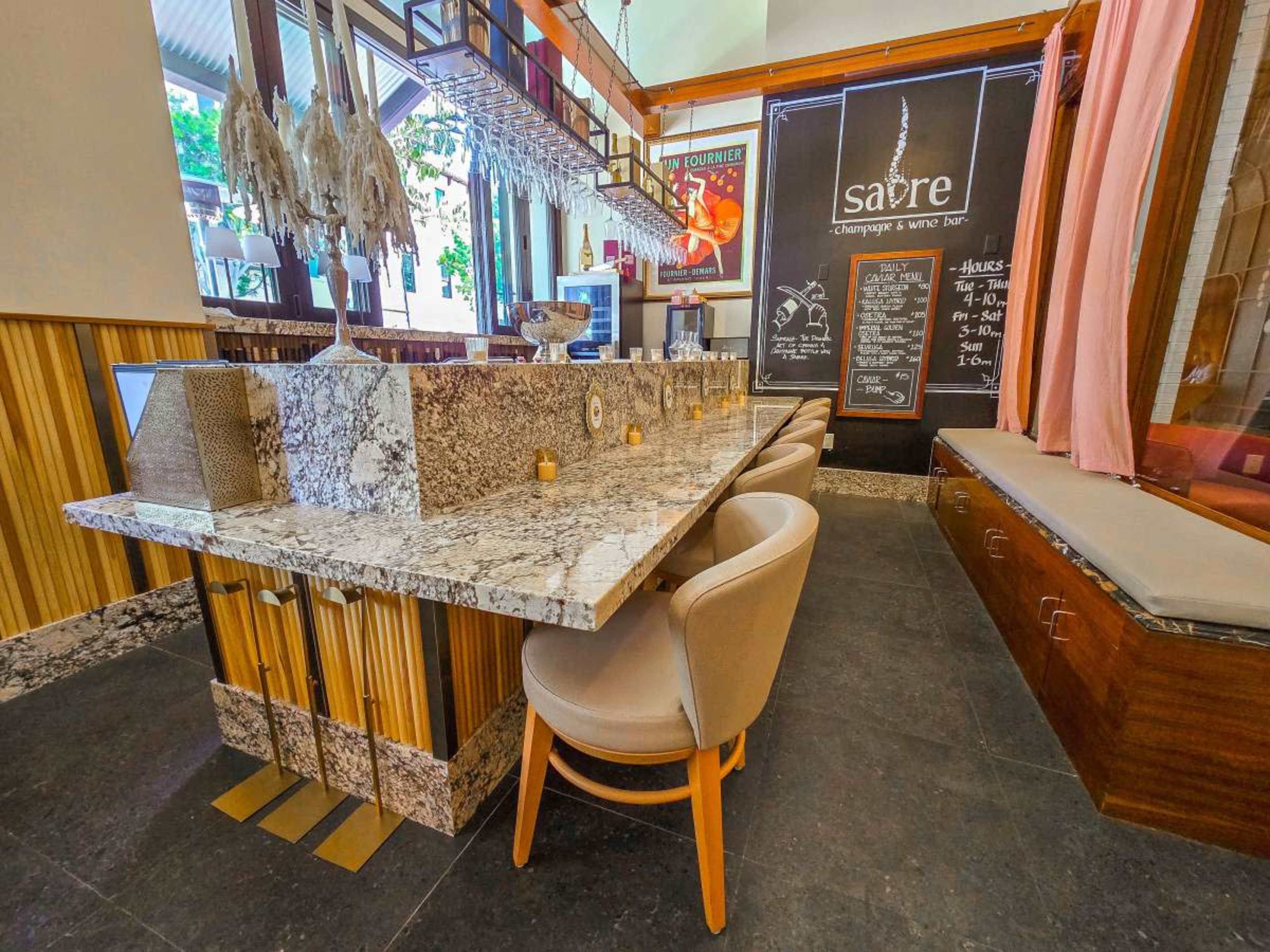 The image shows a modern bar area with a granite countertop, high stools, and a stylish interior featuring wooden accents and a chalkboard menu.