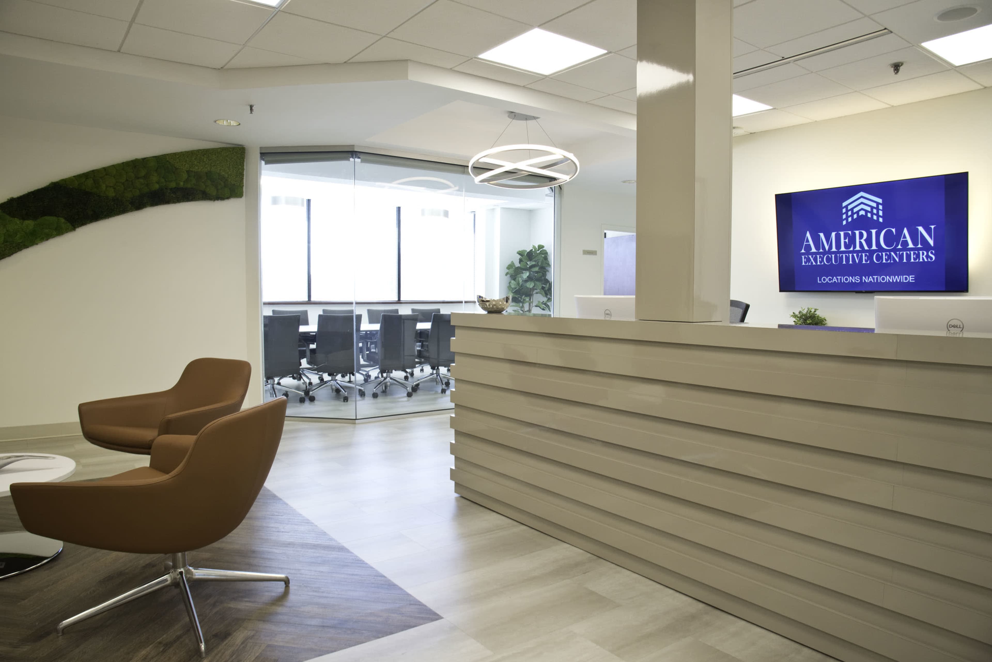 A modern office reception area with a sleek front desk, two brown chairs, and a conference room visible in the background.