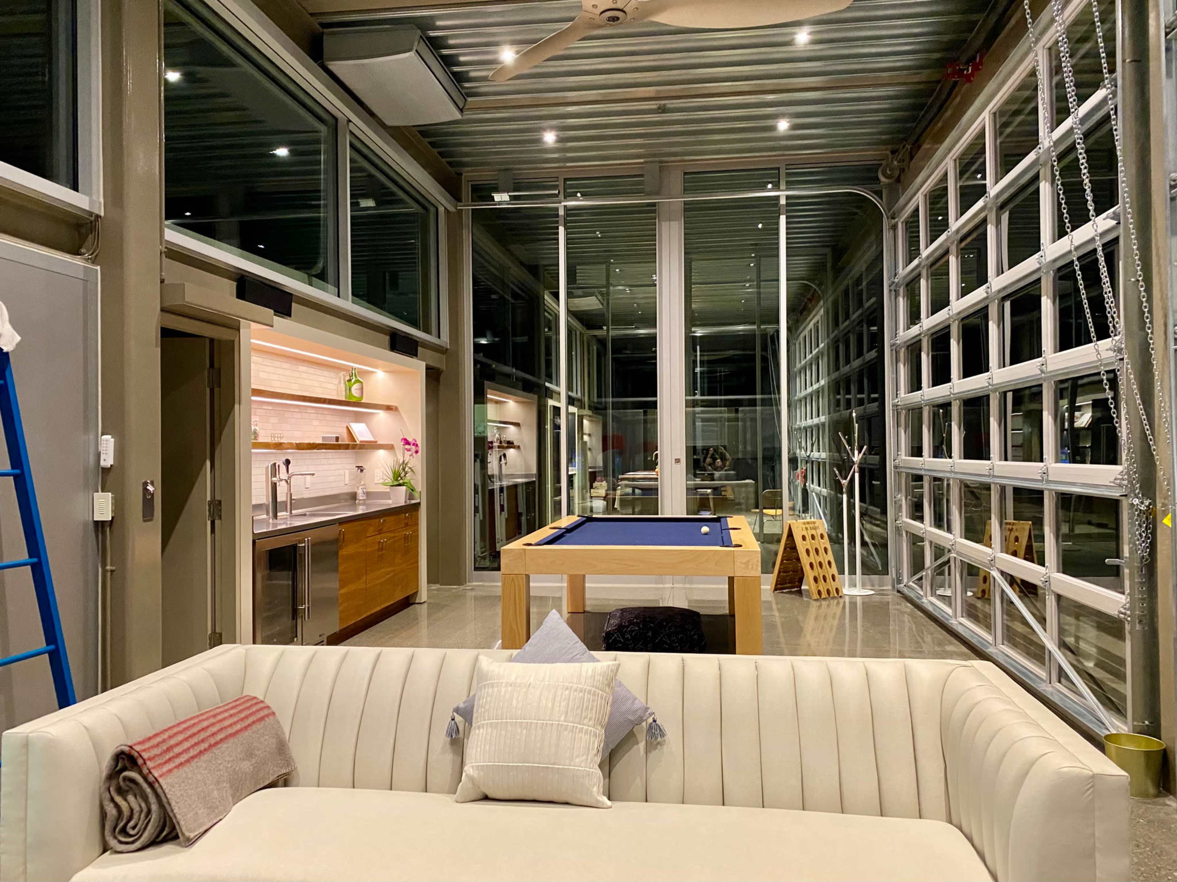 An open-concept living space with large glass doors, a pool table, a modern kitchen, and a white sectional sofa.