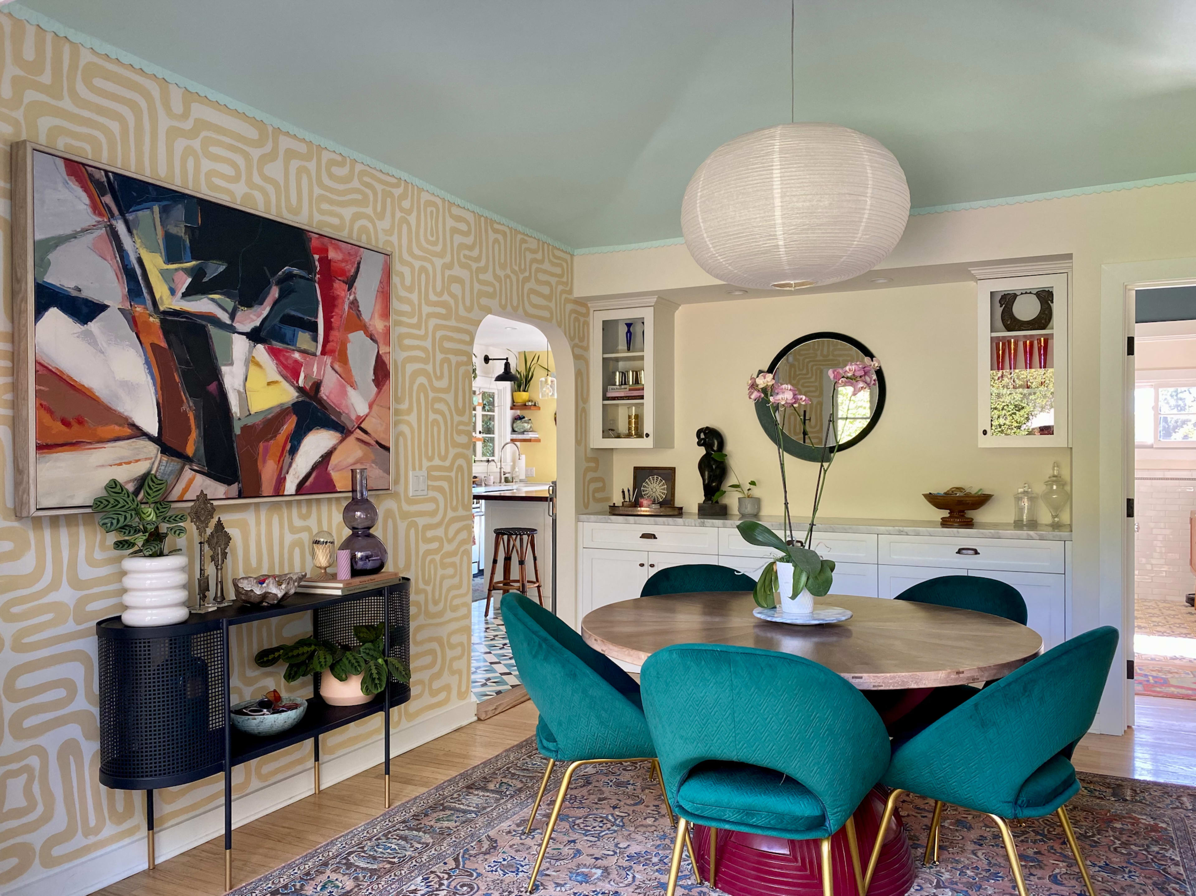 A modern dining area featuring a round table surrounded by green chairs, alongside a patterned wall and a large piece of abstract art.