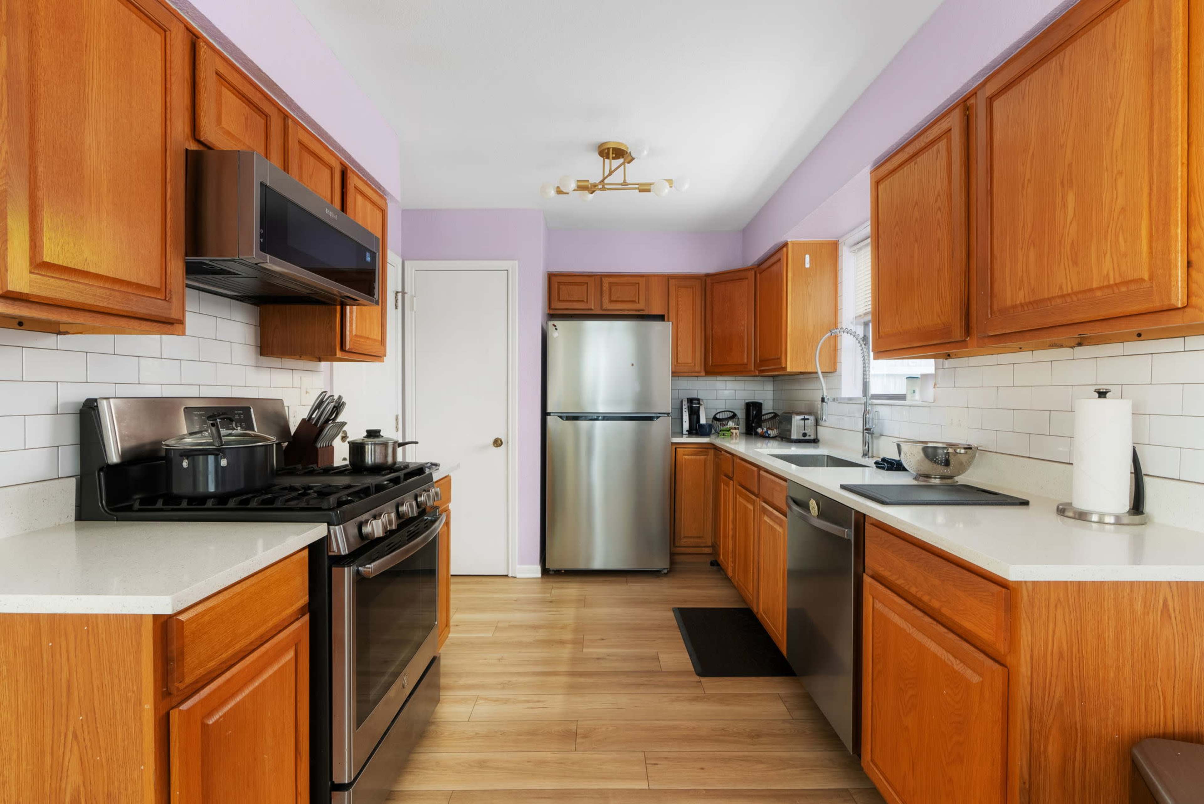 The image shows a modern kitchen featuring wooden cabinets, stainless steel appliances, and a counter with a sink and stove.