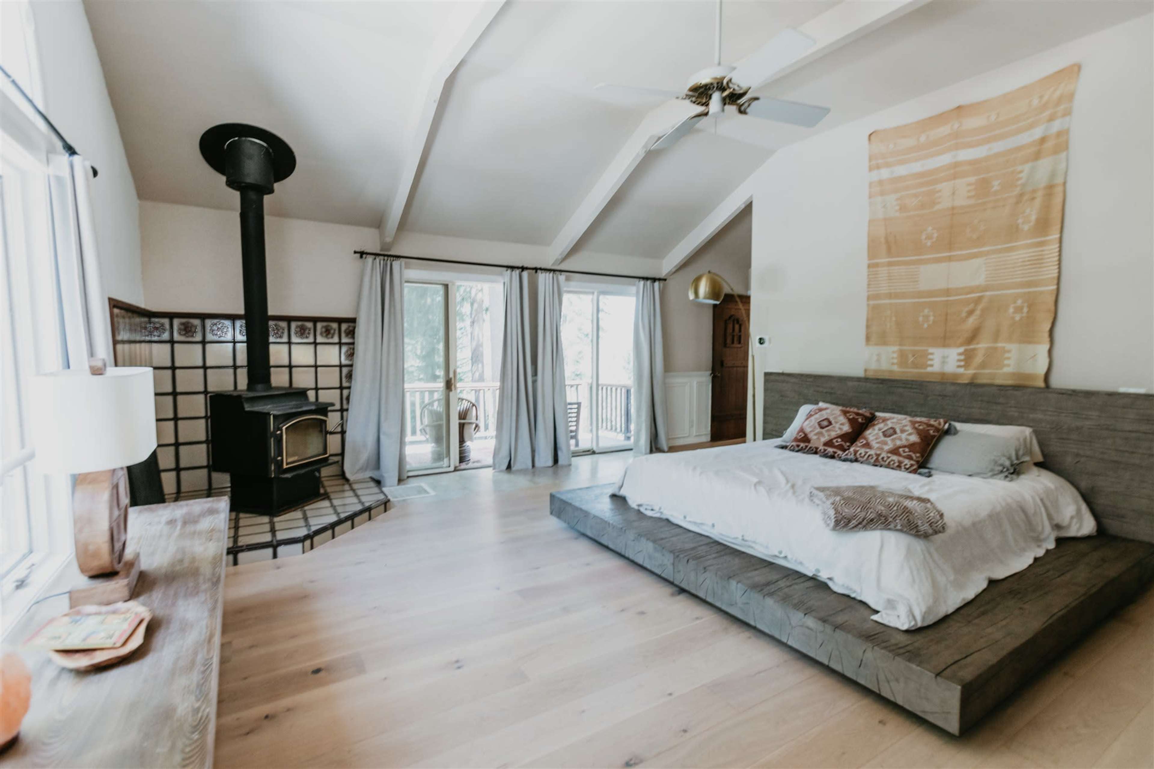A spacious bedroom with a large platform bed, a cozy wood stove, and sliding glass doors leading to a balcony.