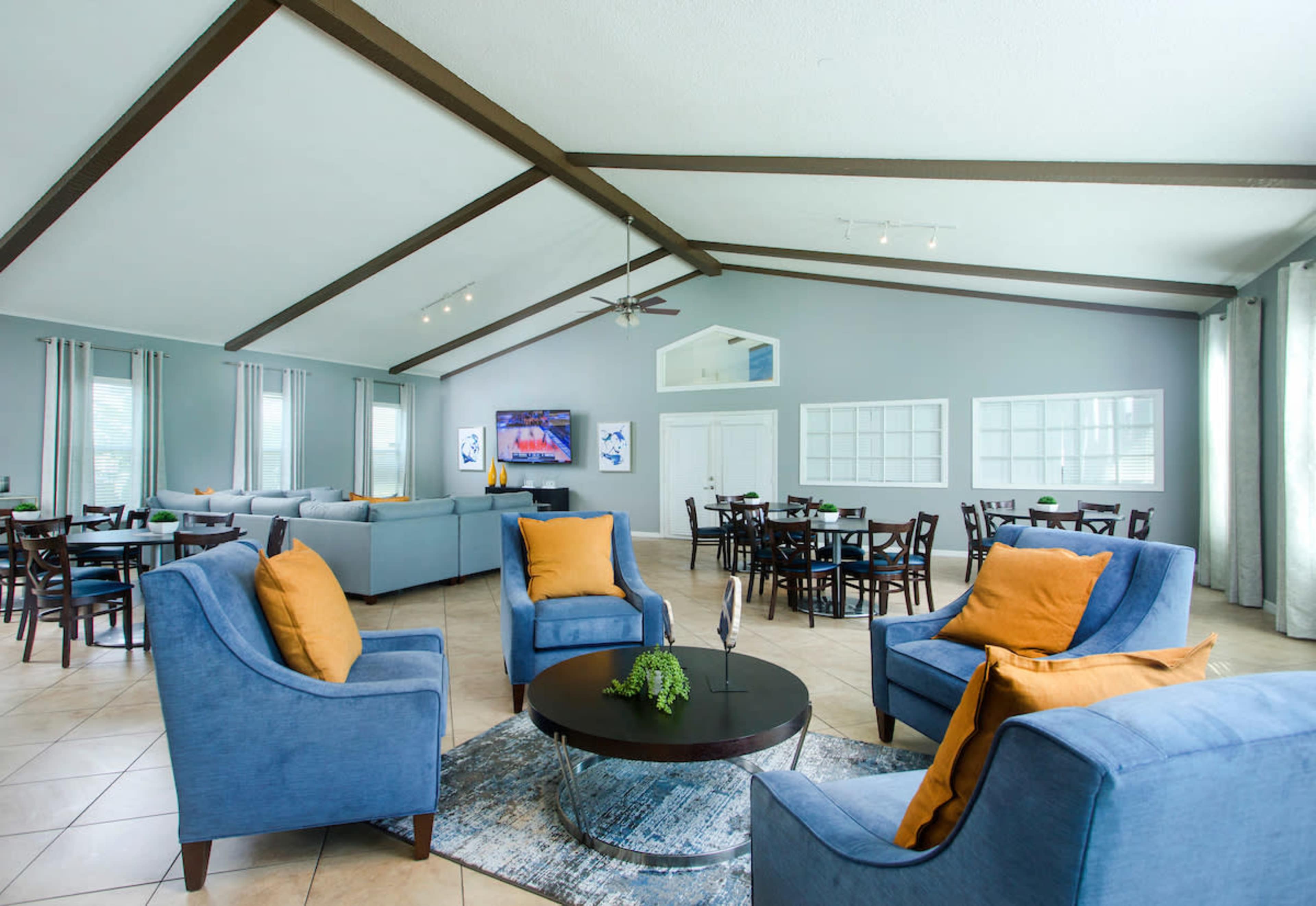 A spacious lounge area with blue armchairs, a round coffee table, and a view of a dining area in the background, featuring tables and chairs.