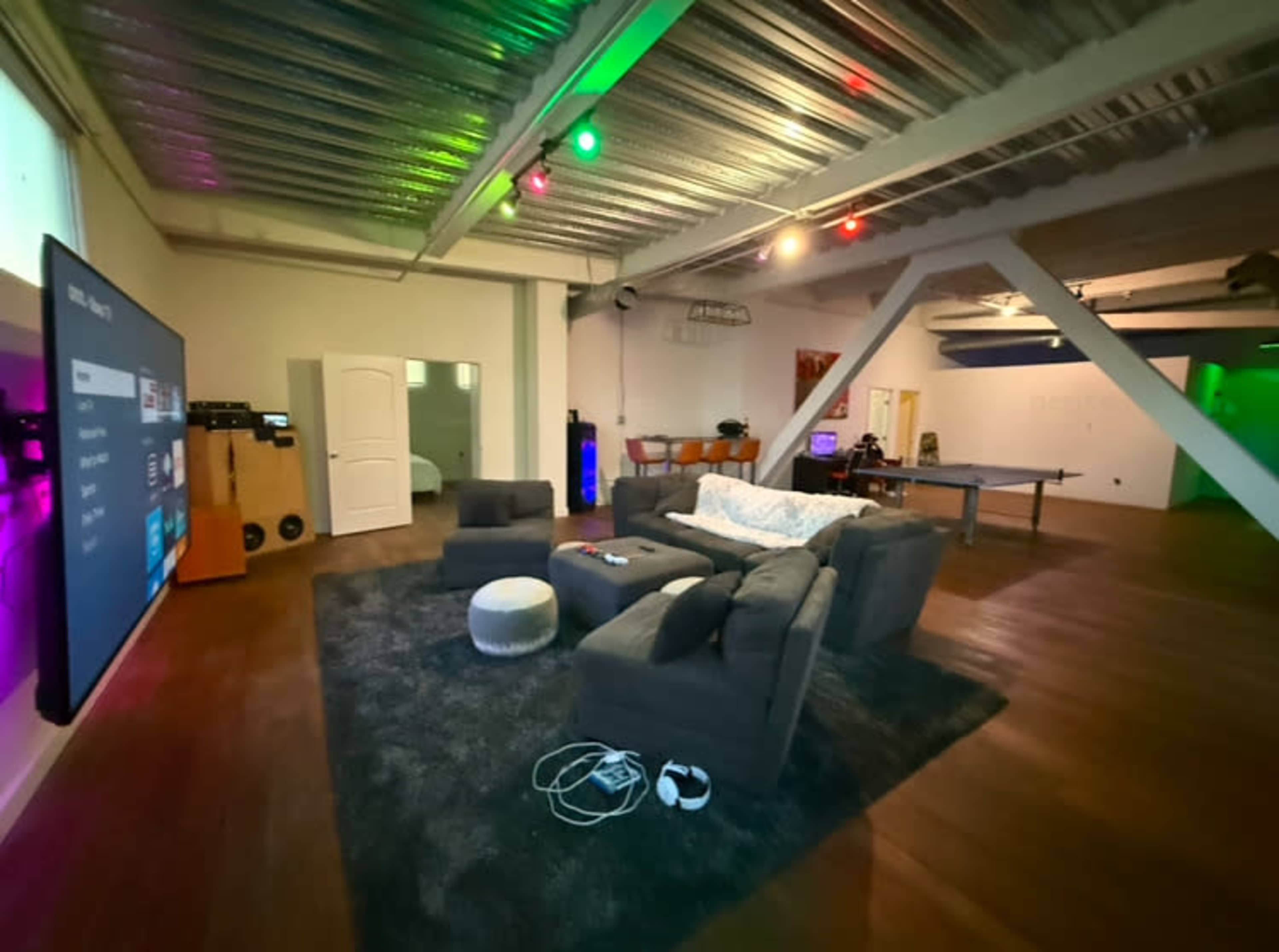 A spacious, modern lounge area features a sectional sofa, a large screen on the wall, and ambient lighting.