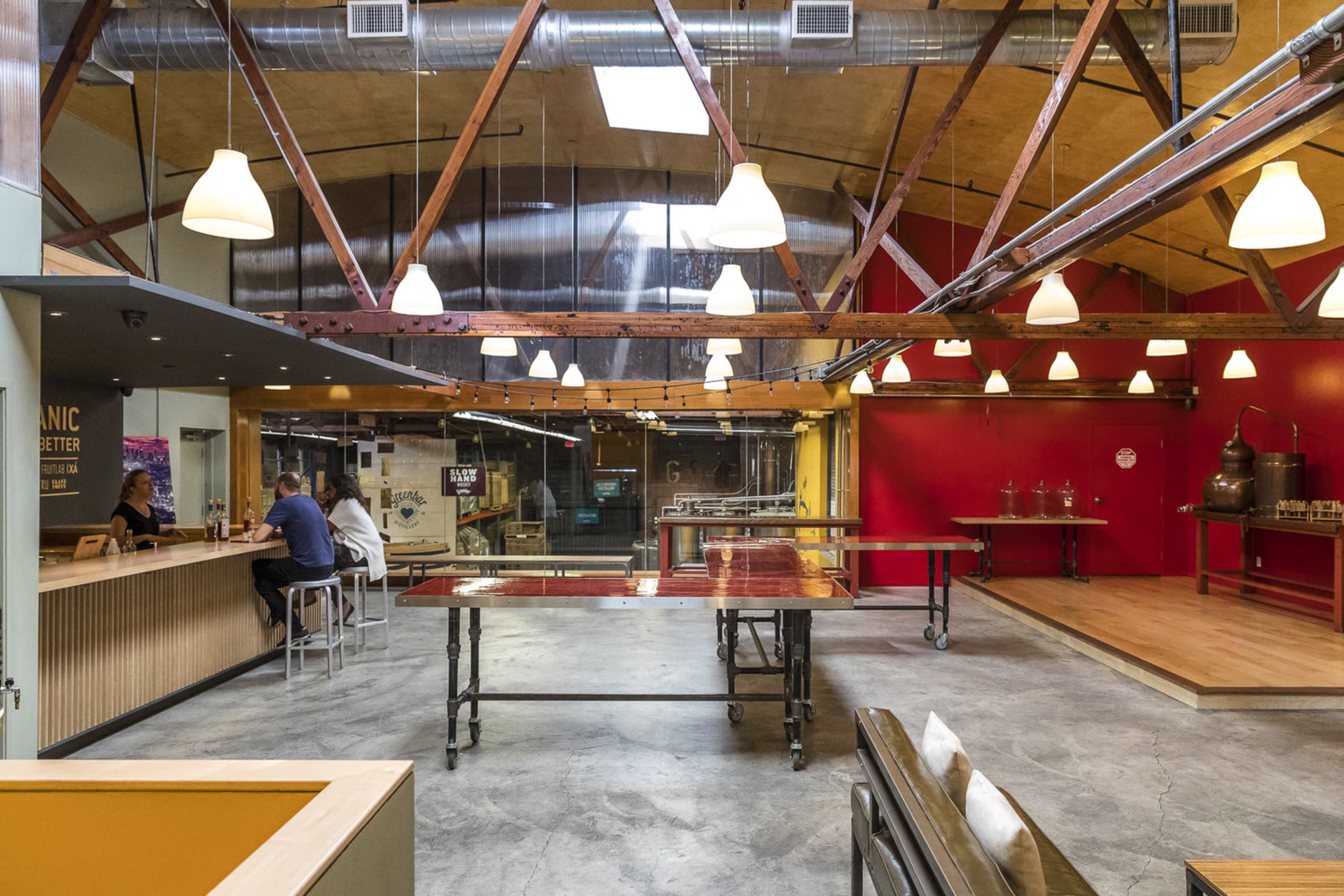 A spacious, modern brewery with exposed wooden beams, large pendant lights, and tables arranged in an open layout.