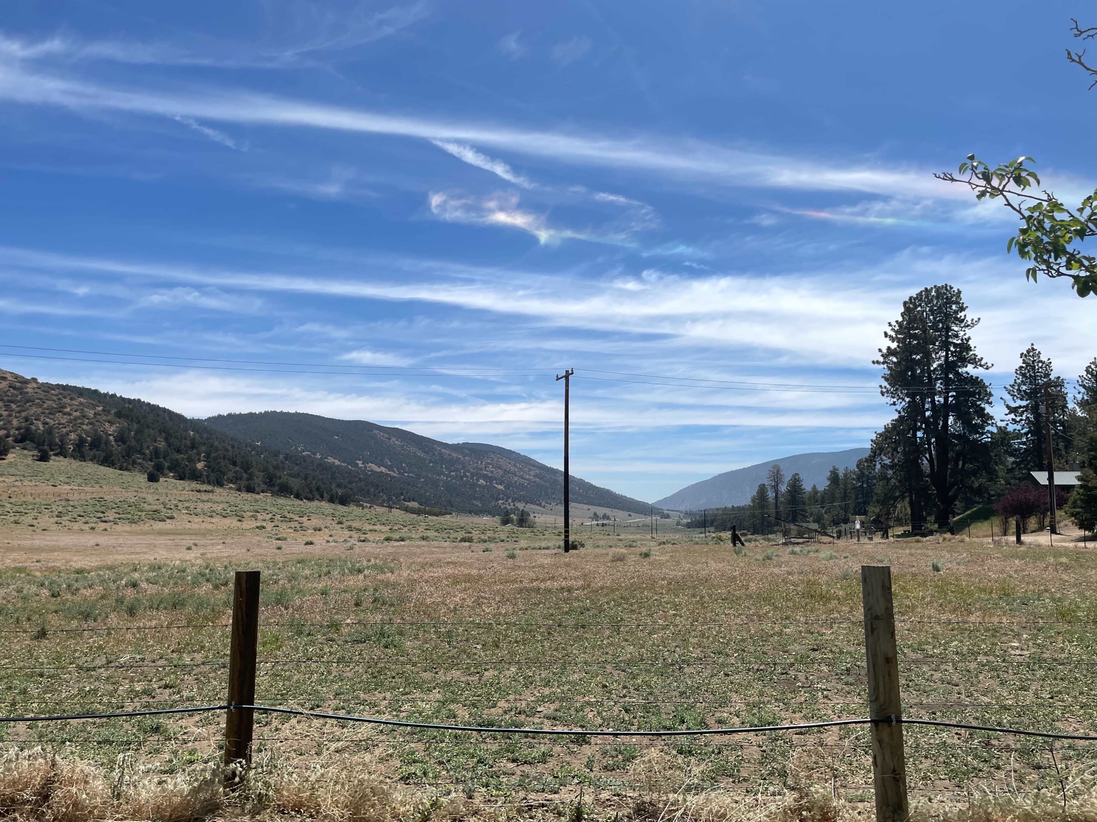 A wide landscape features rolling hills and a clear blue sky with wispy clouds, intersected by a power line and sparse vegetation.