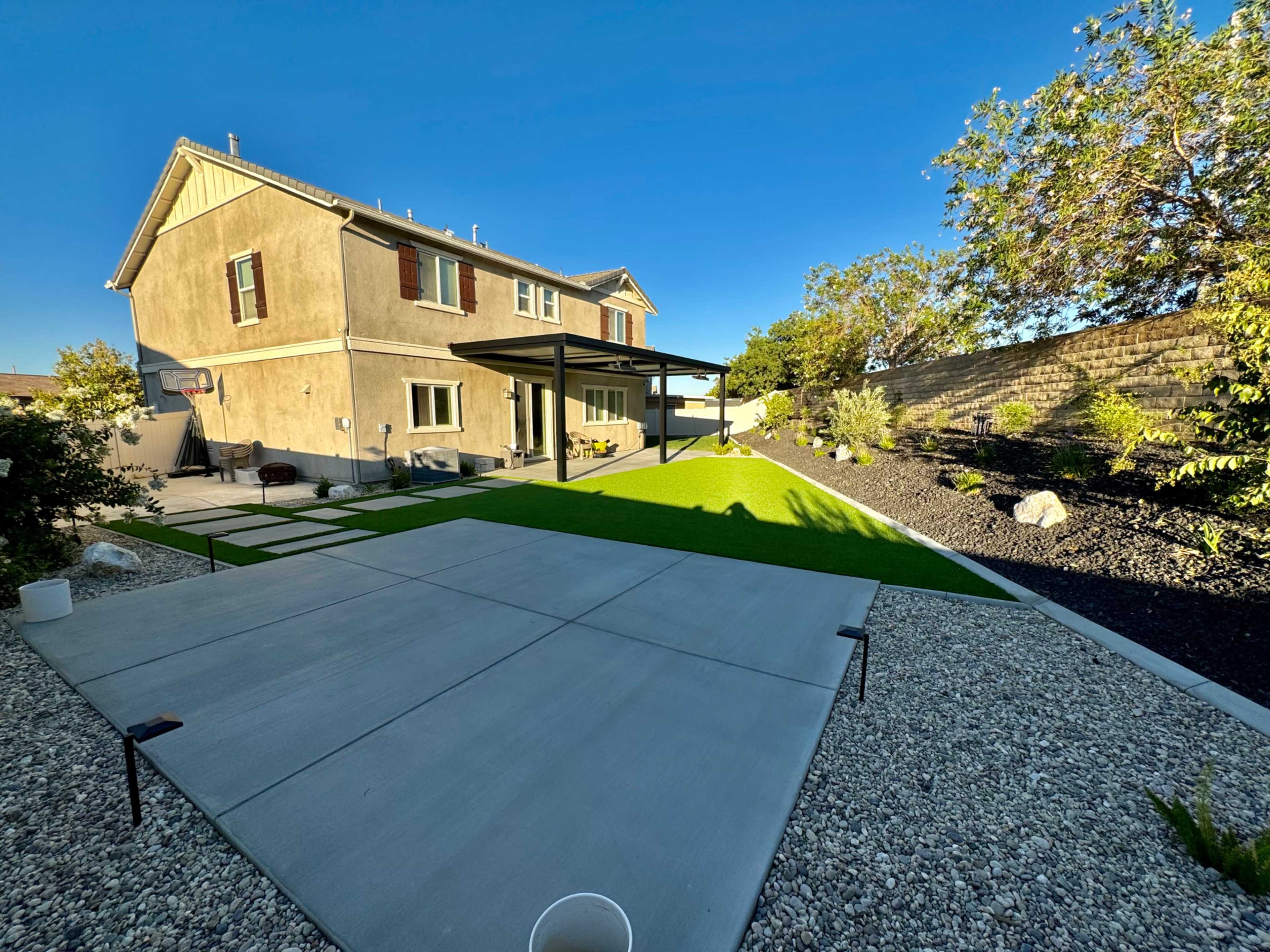 A backyard with a concrete patio, artificial grass, and a two-story house with a covered porch.