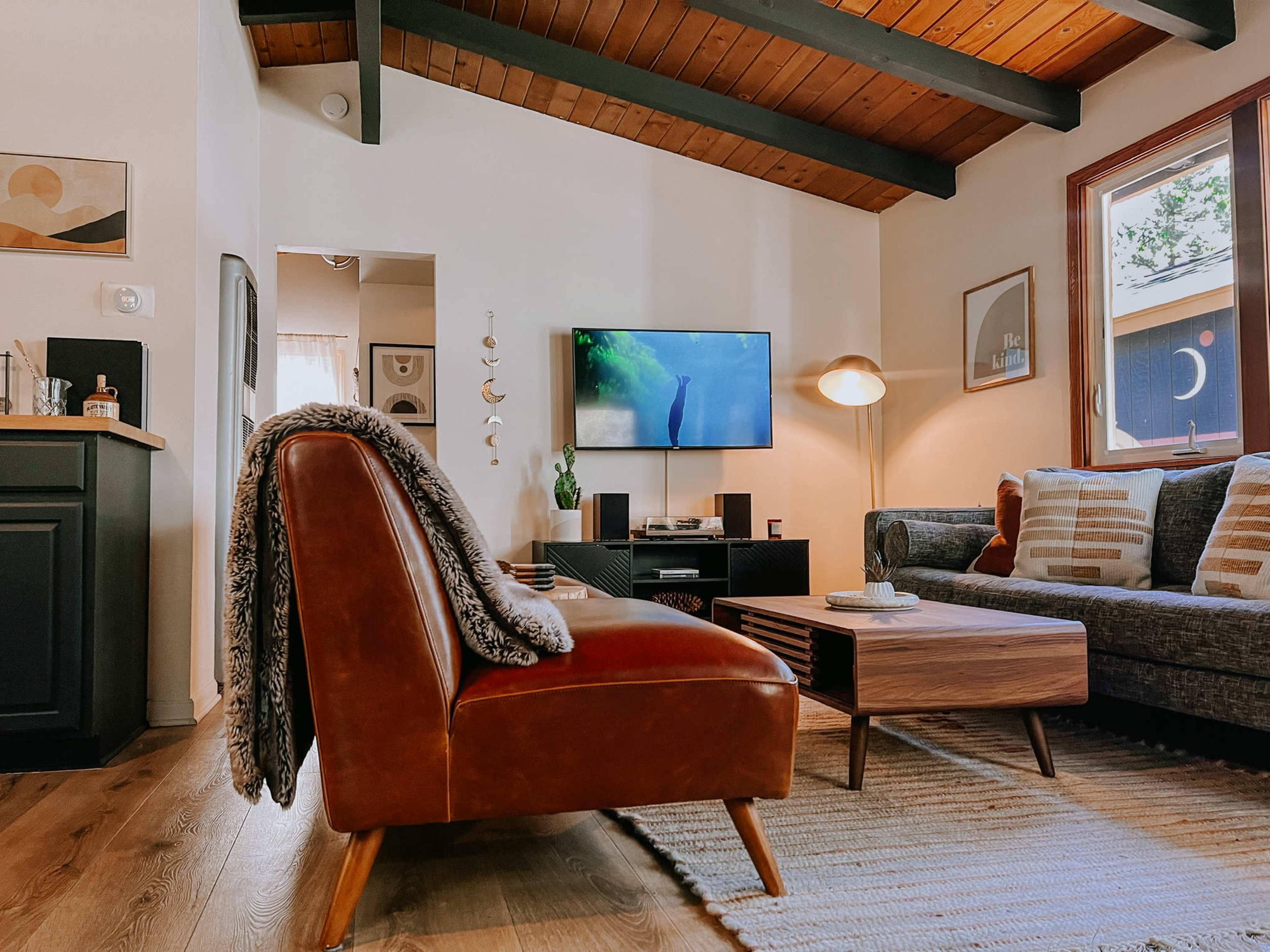A living room features a leather sofa and a coffee table, with a television mounted on the wall and a cozy rug on the wooden floor.