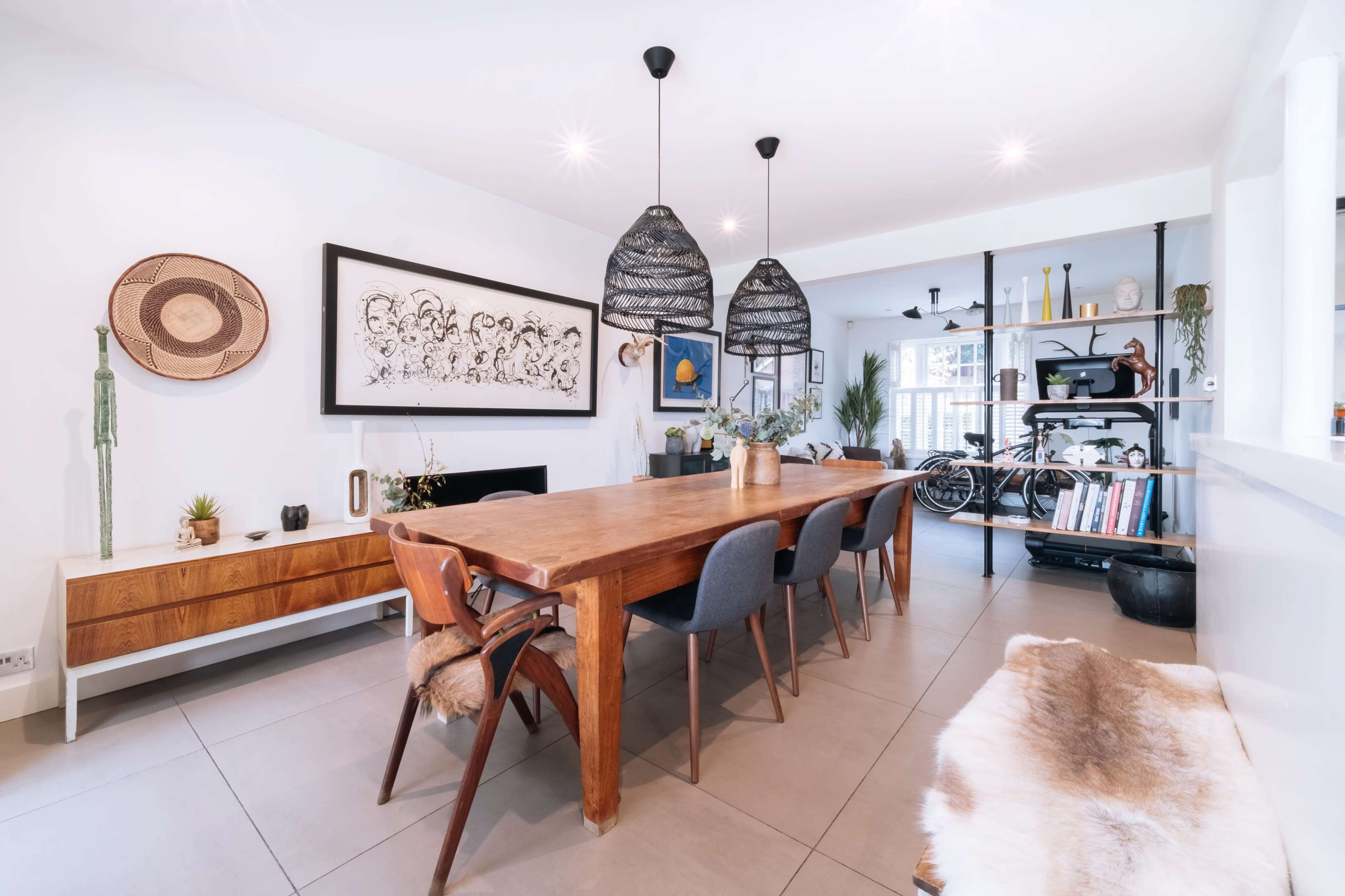 A spacious dining area features a large wooden table surrounded by upholstered chairs, decorative wall art, and modern pendant lighting.