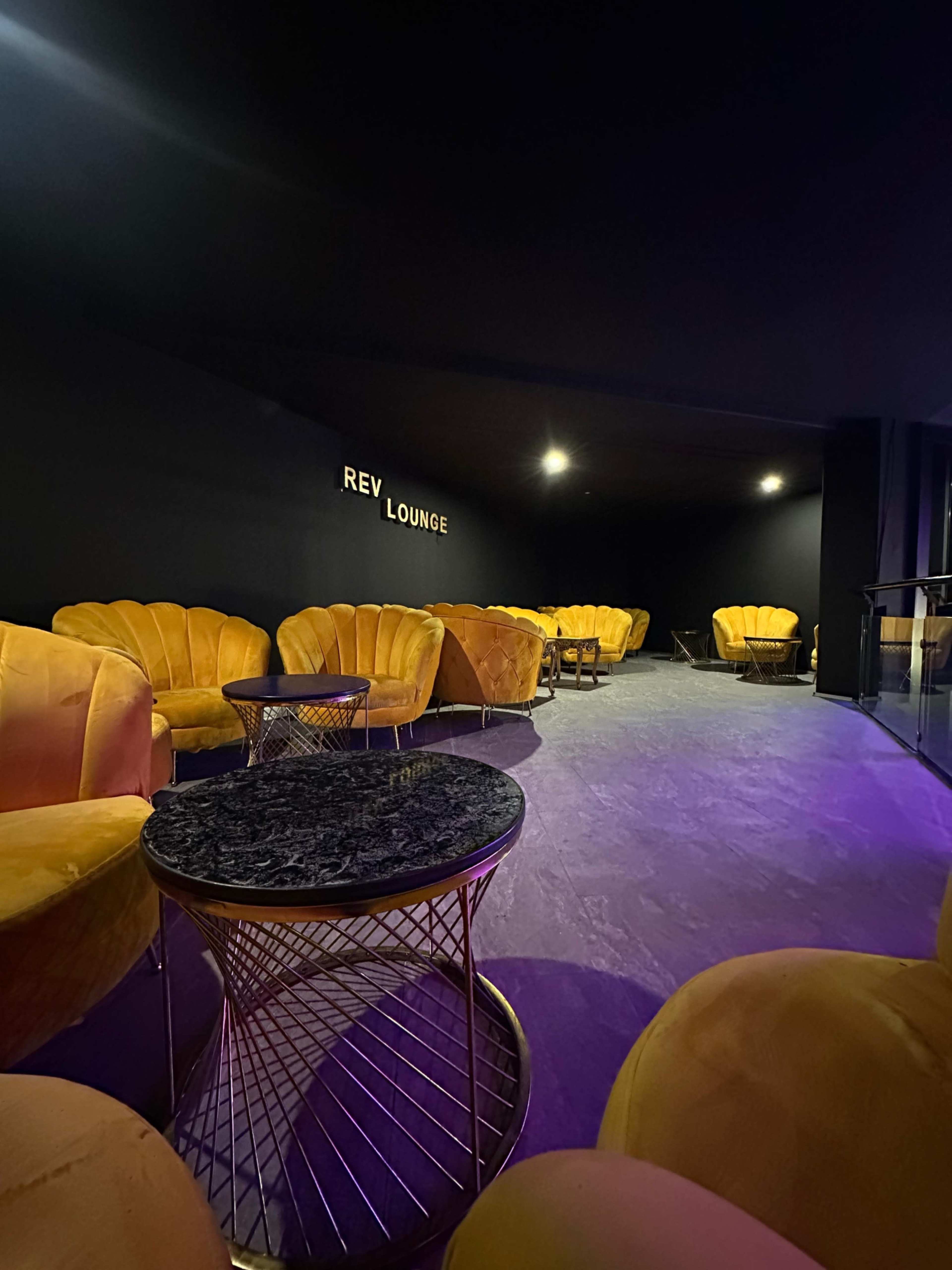 The image shows a modern lounge area with yellow velvet chairs and a dark table against a black wall.