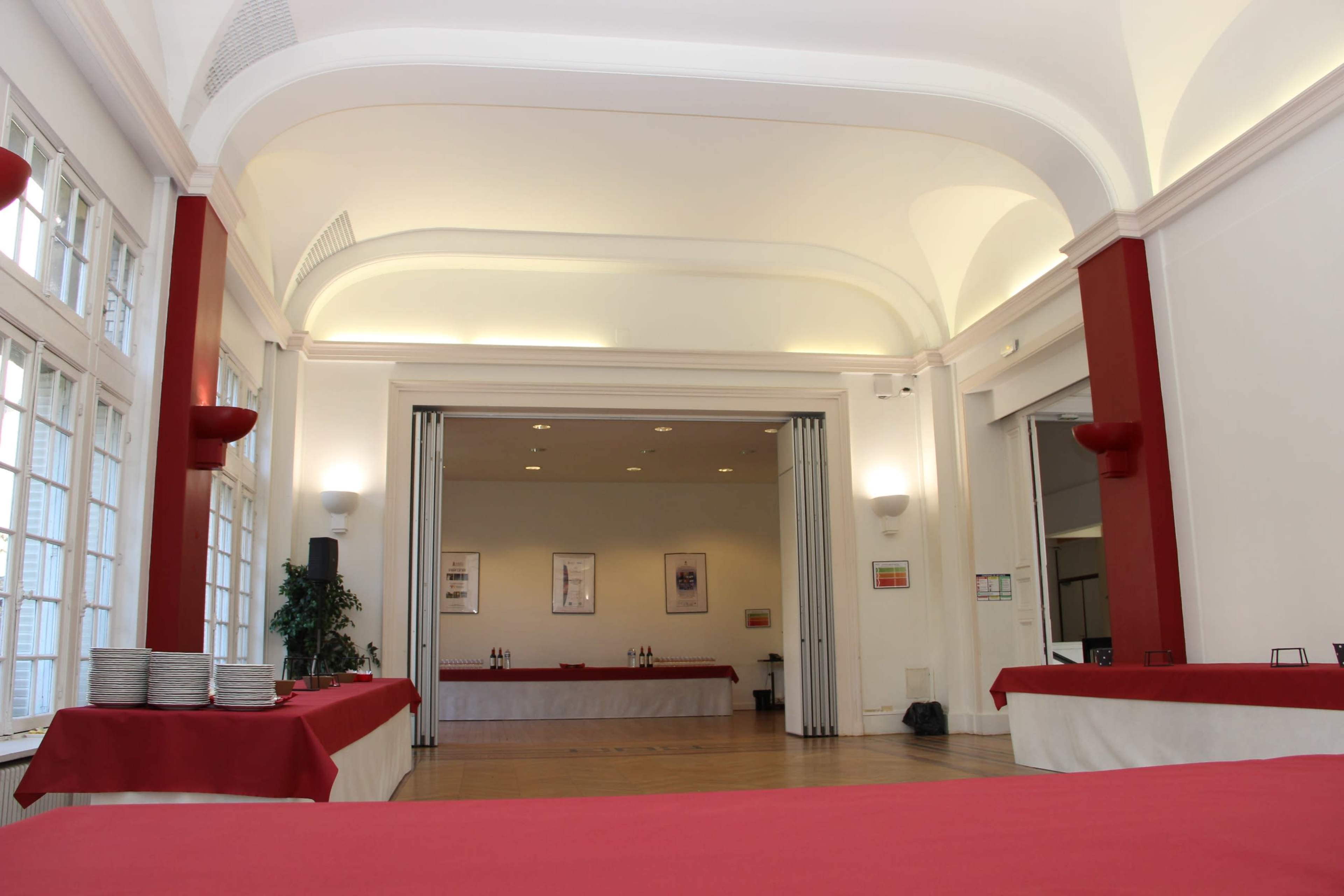 A spacious event hall featuring red-accented decor, tables covered with white and red cloth, and a dividable area in the background.