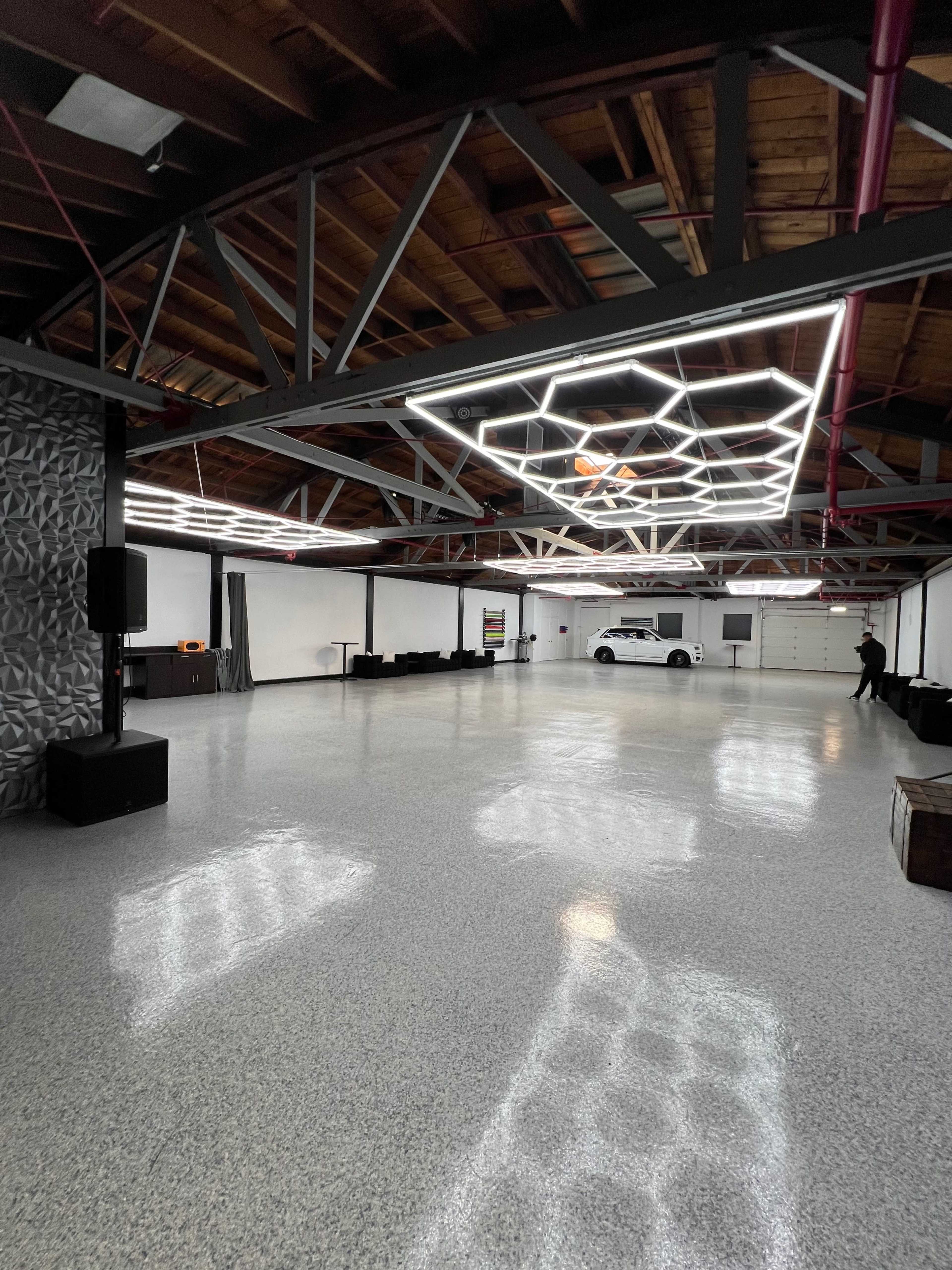 A spacious, modern interior with polished flooring, a geometric light fixture on the ceiling, and minimal furnishings.