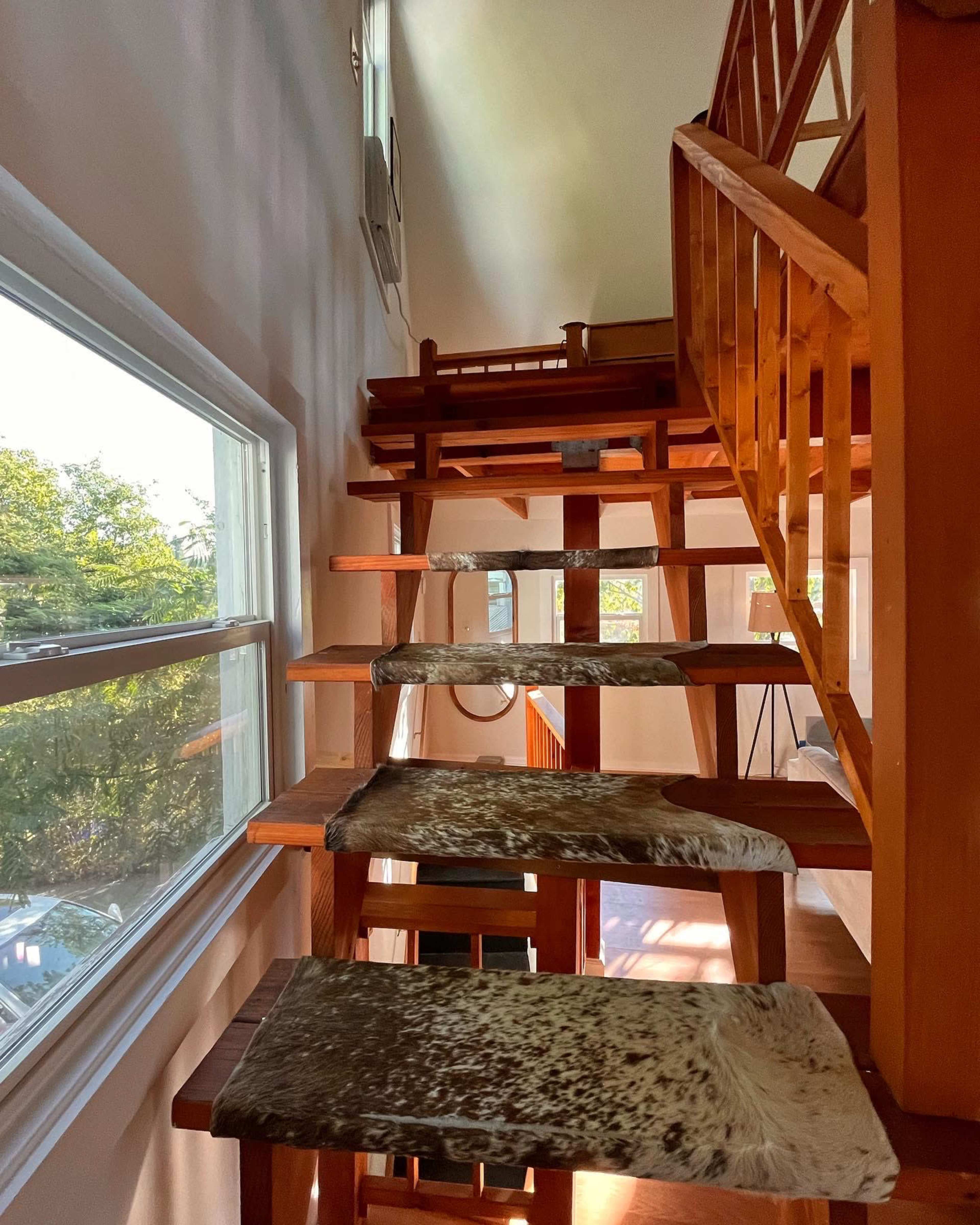 A wooden staircase with open risers and cowhide-covered steps leads to an upper level in a well-lit interior space.