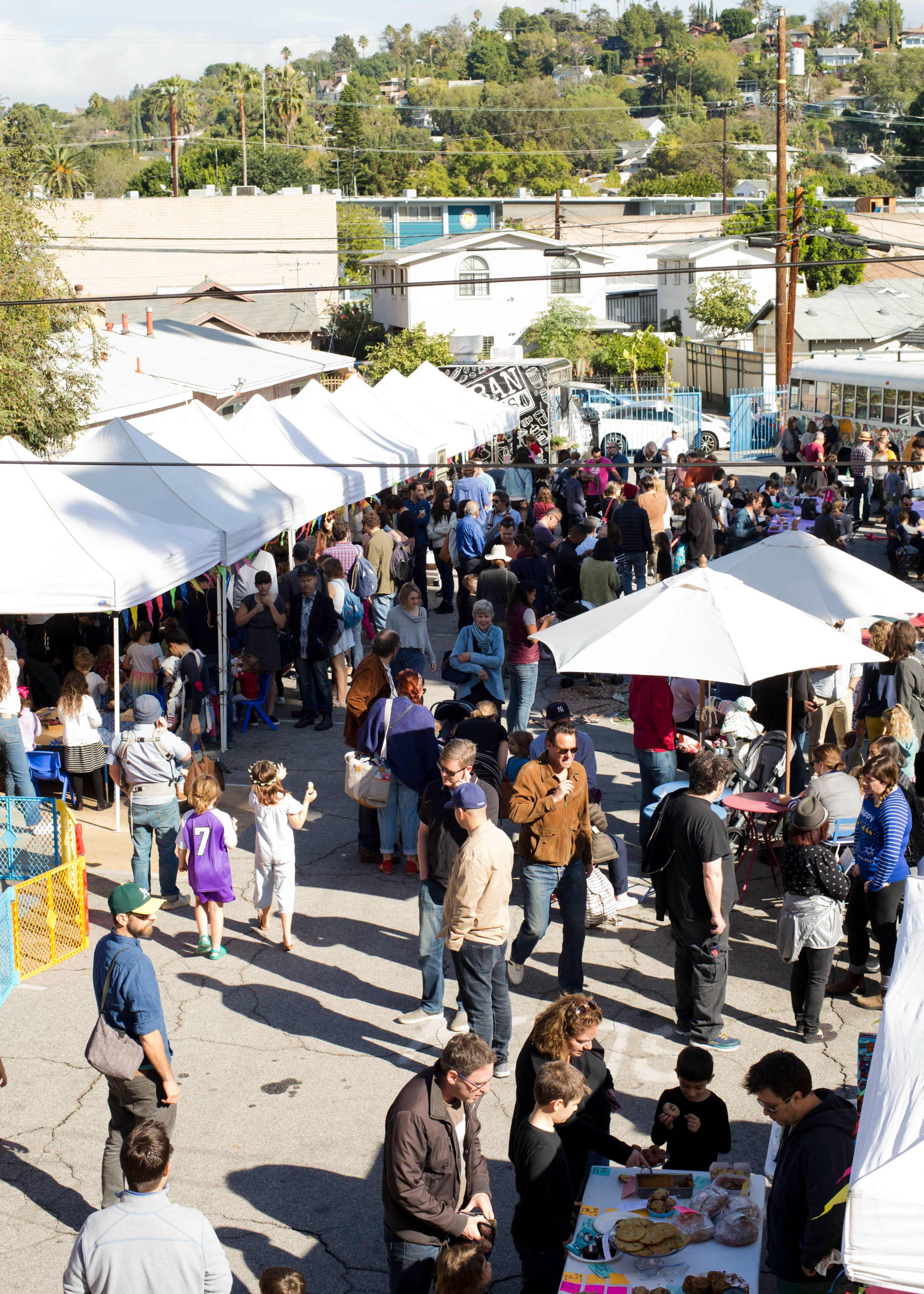 A bustling outdoor event features numerous tents and a large crowd of people engaging in various activities.