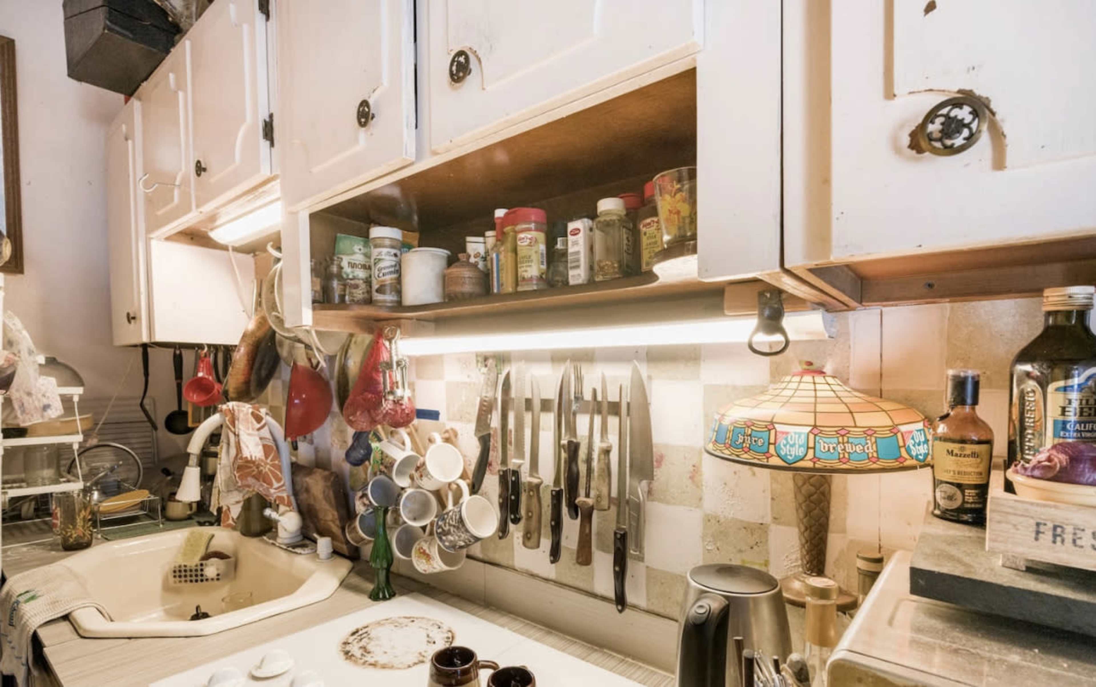 A kitchen with overhead cabinets, a shelf of spices, a knife block, and a colorful lamp above the counter.
