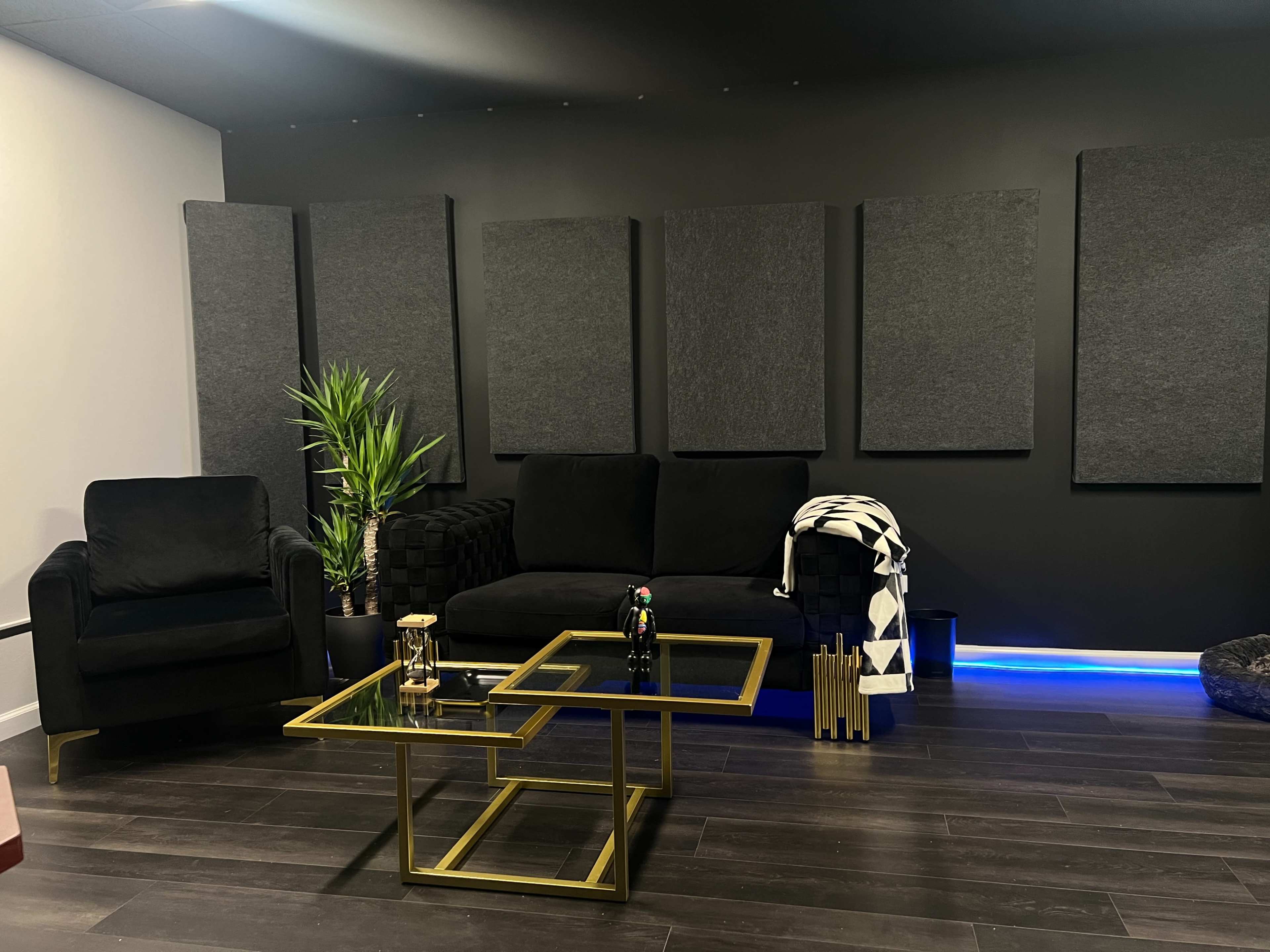 A modern lounge area with black furniture, a glass coffee table, and decorative soundproof panels on the walls.