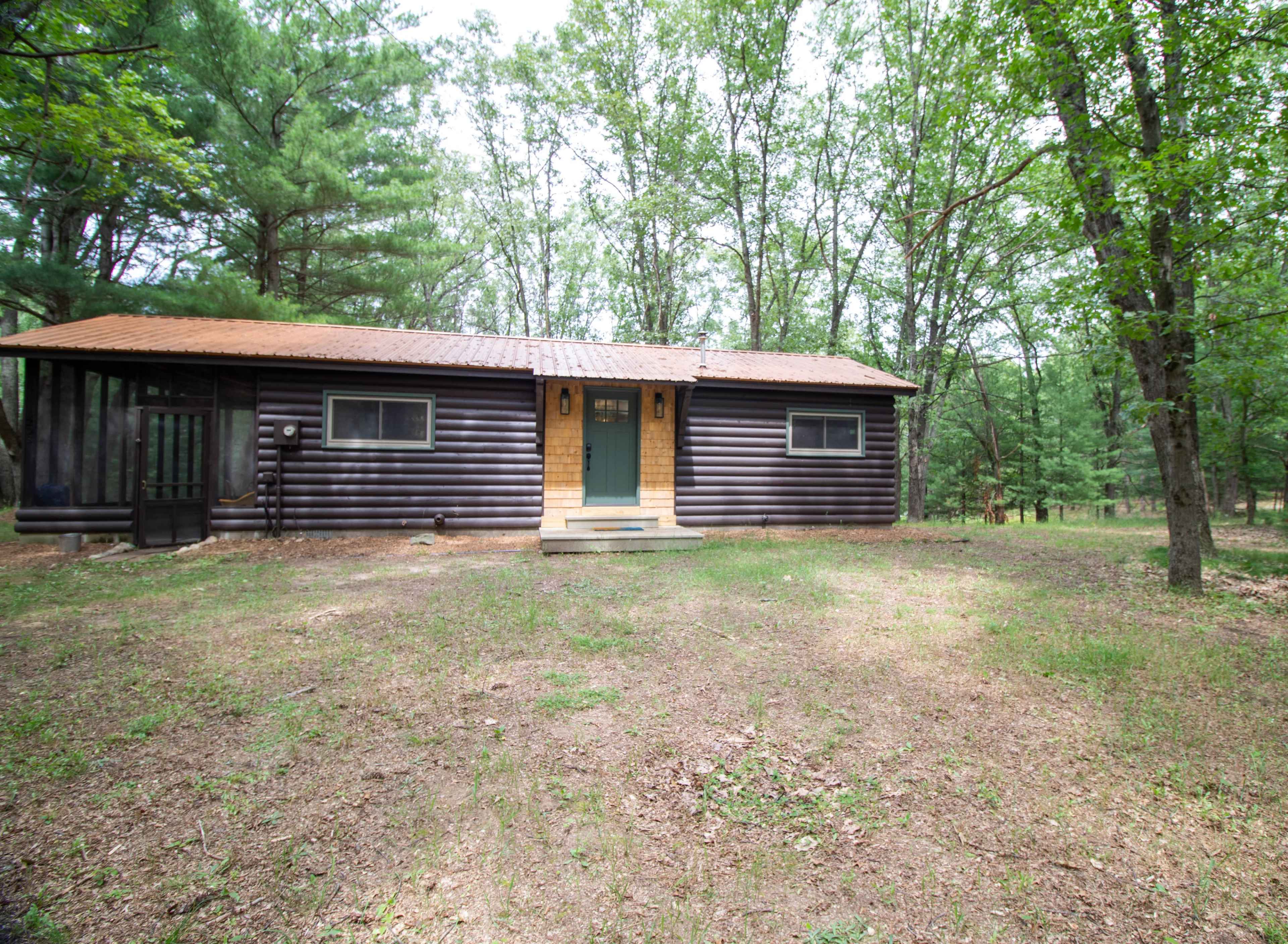 A single-story log cabin with a green door is situated among trees in a wooded area.