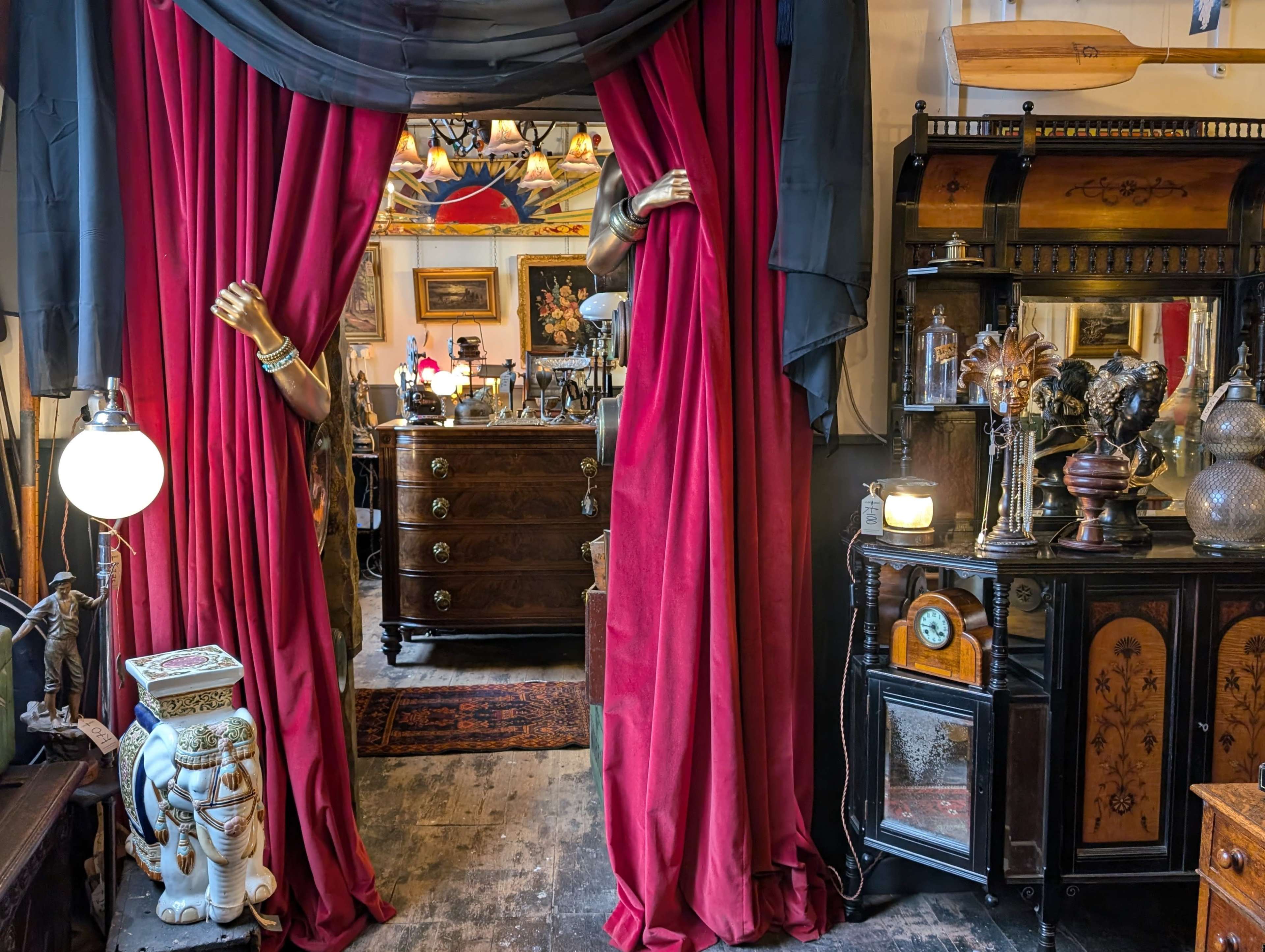 The image shows a vintage antique shop entrance draped with red curtains, revealing carefully arranged furniture and decorative items inside.