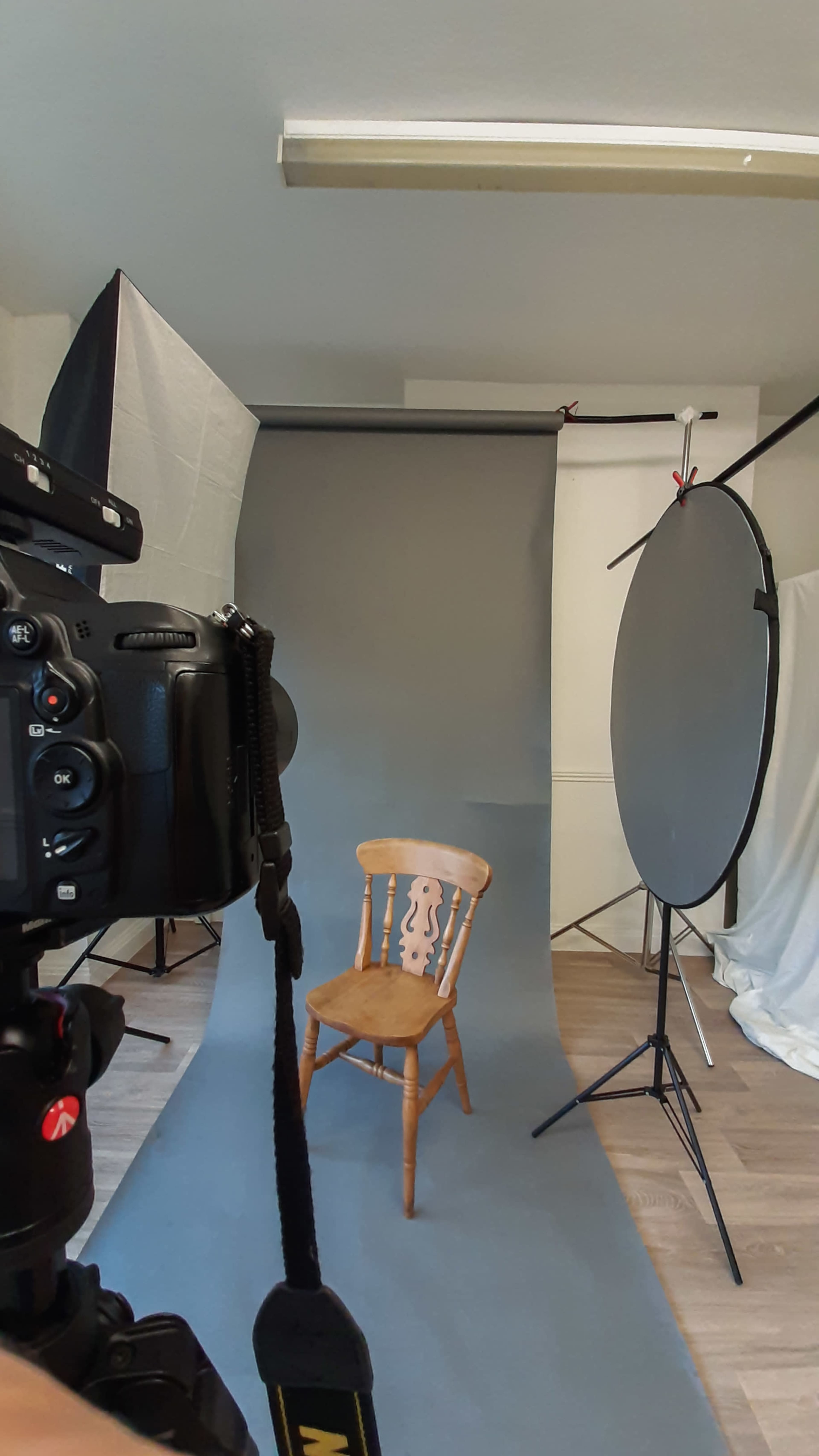 The image shows a photography setup featuring a wooden chair in front of a gray backdrop, alongside a camera and lighting equipment.